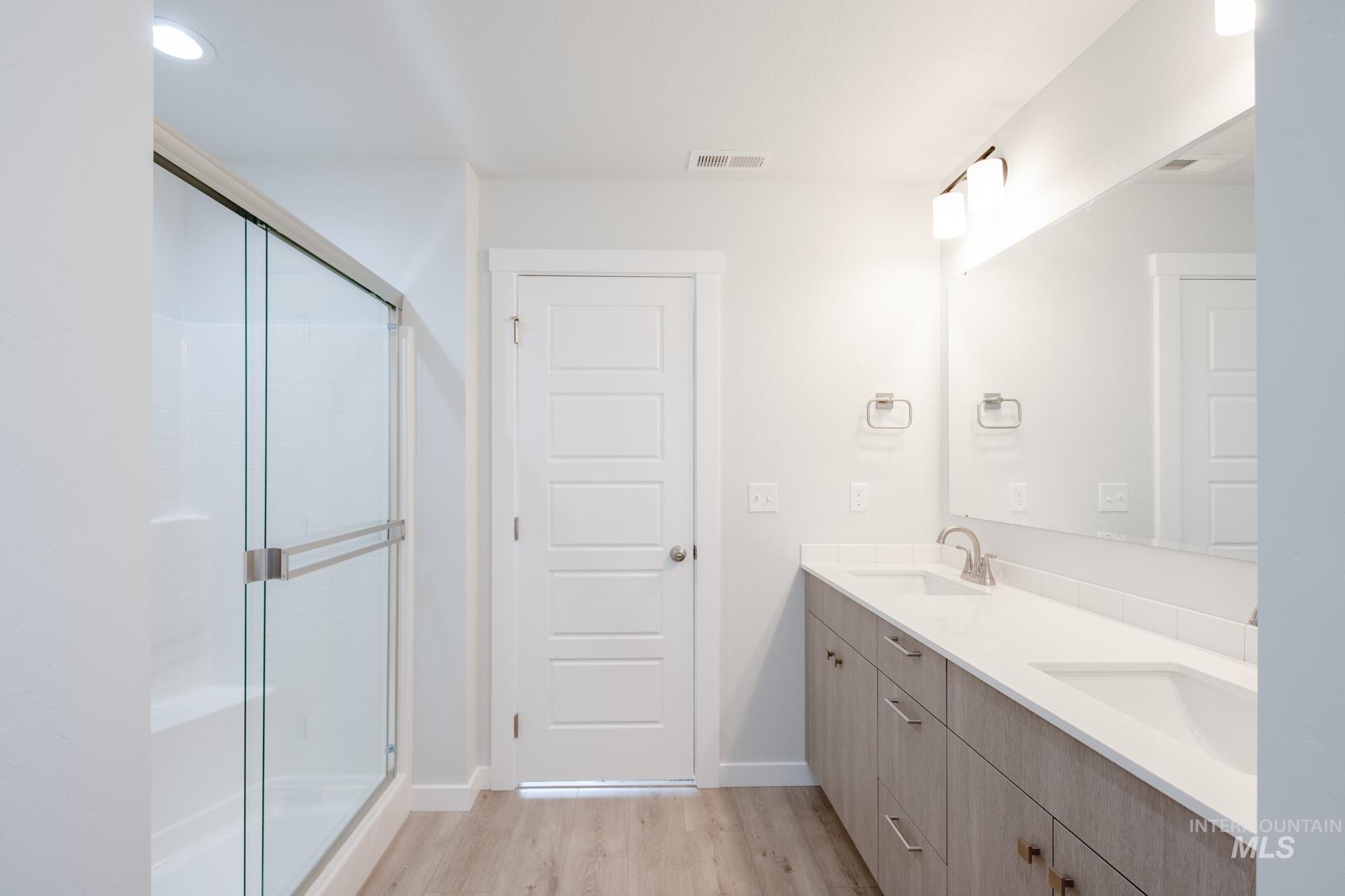 Bathroom featuring light wood-style flooring, double vanity, a stall shower, and recessed lighting