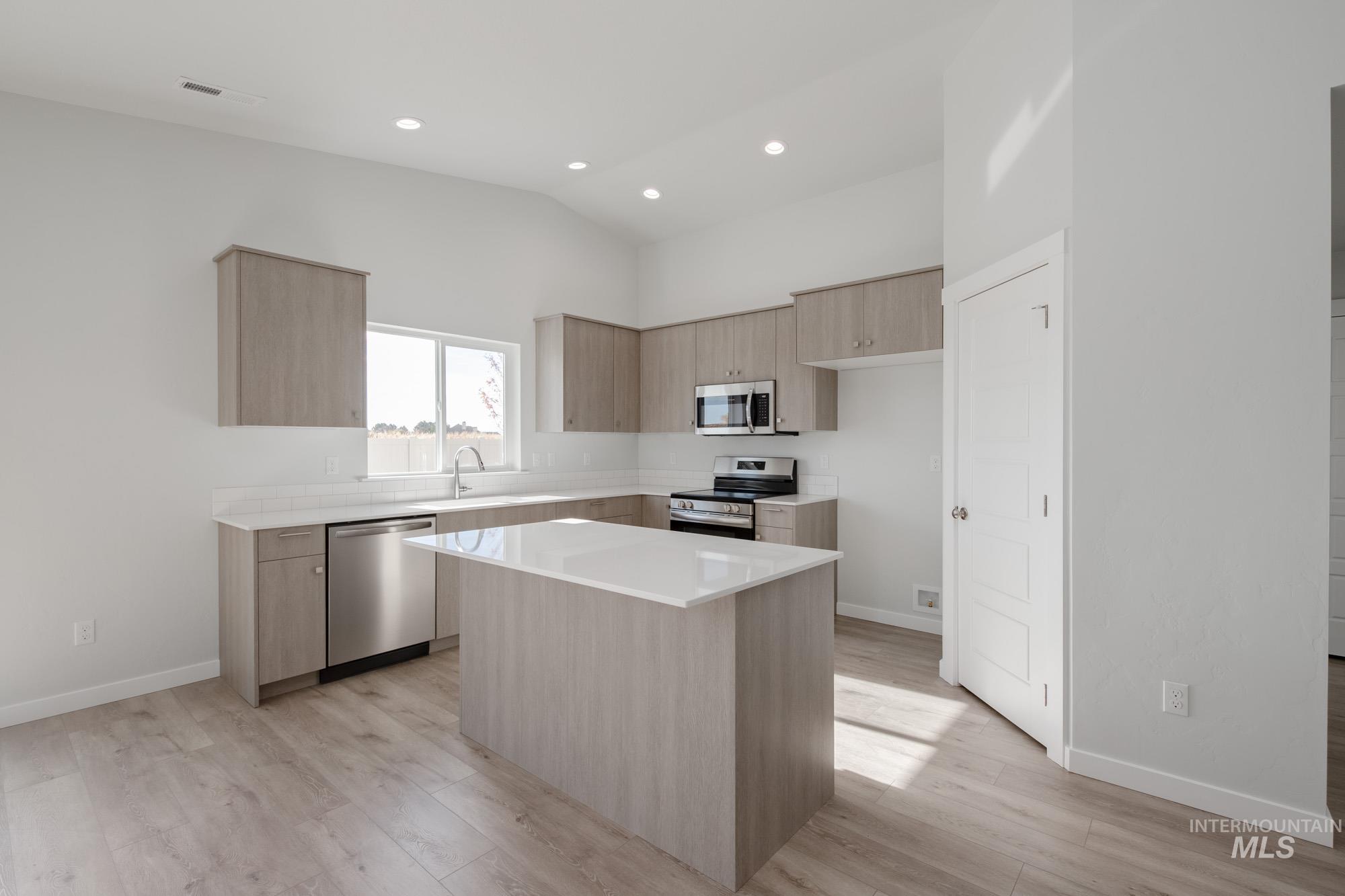 Kitchen featuring light brown cabinetry, modern cabinets, stainless steel appliances, a kitchen island, and light wood-style floors