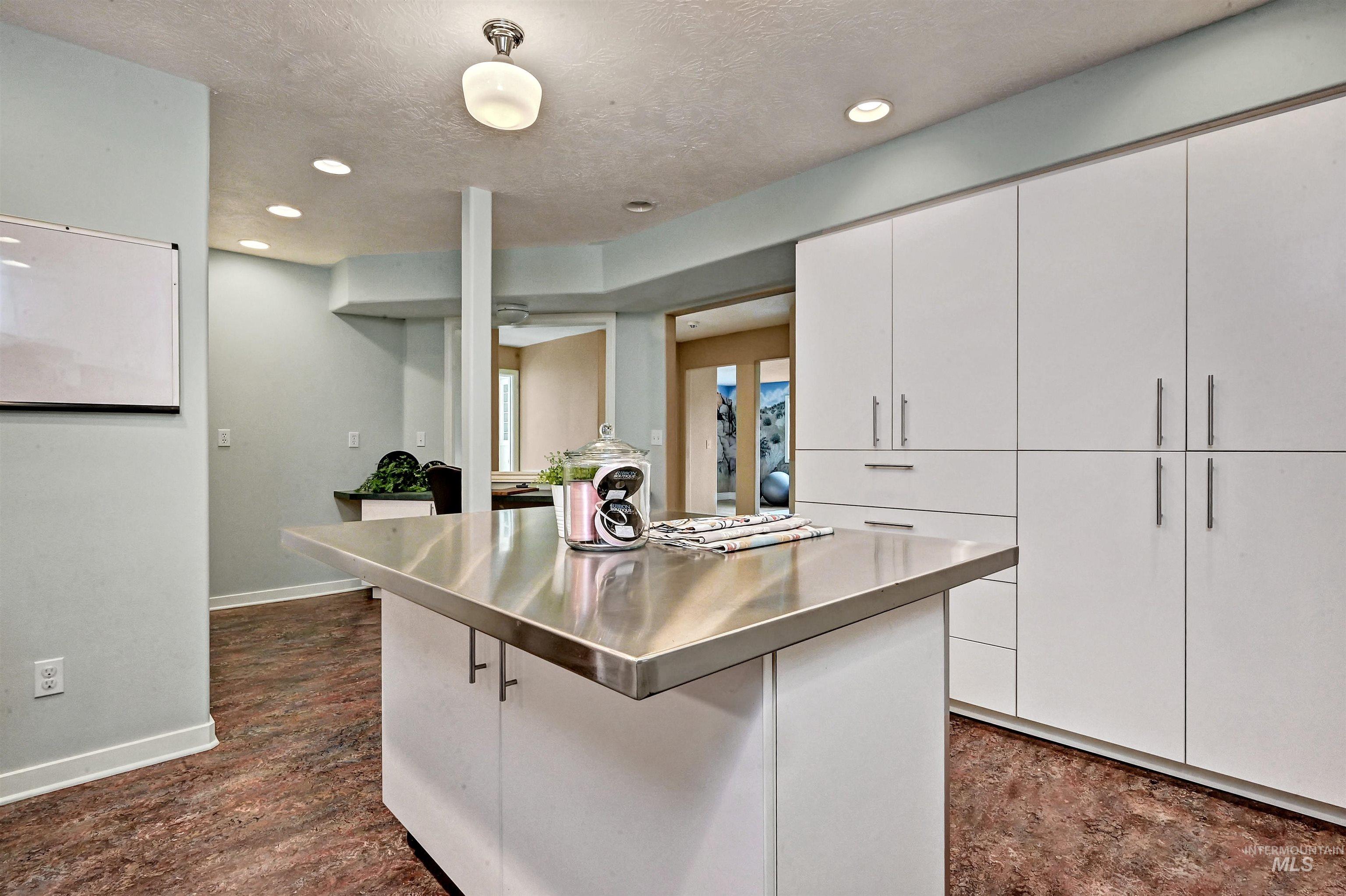 Kitchen with stainless steel countertops, a center island, white cabinetry, a textured ceiling, and recessed lighting