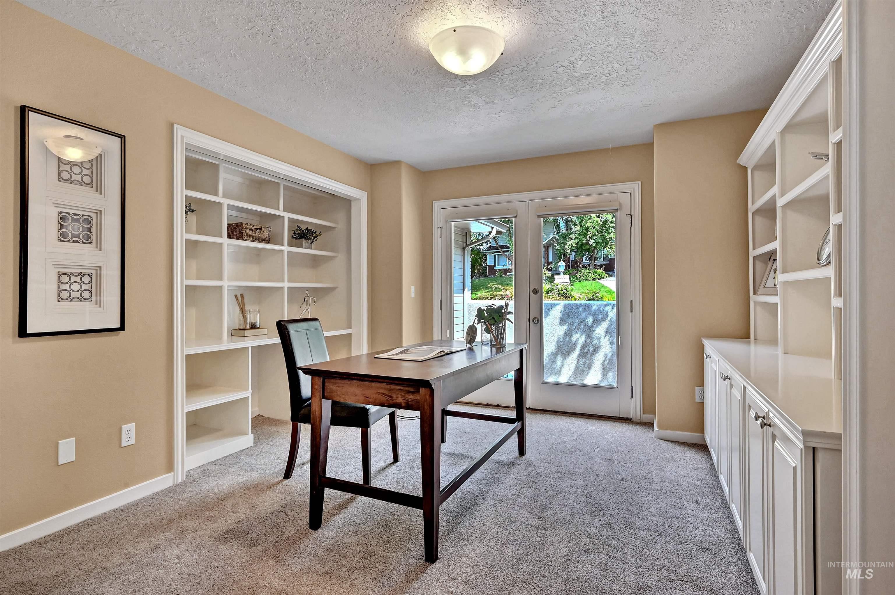 Office with built in shelves, light colored carpet, french doors, and a textured ceiling