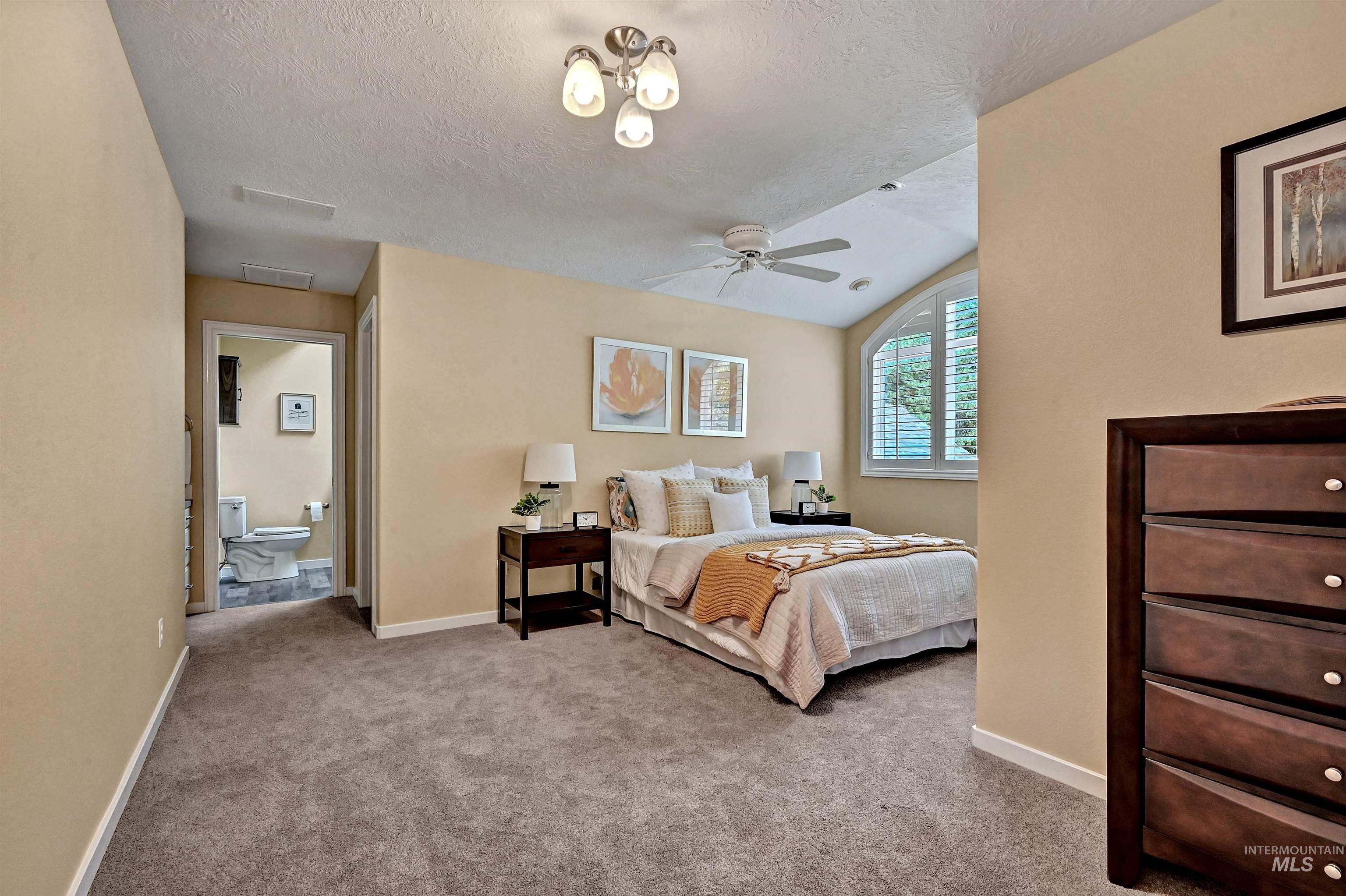 Carpeted bedroom with a textured ceiling, ceiling fan, and ensuite bathroom