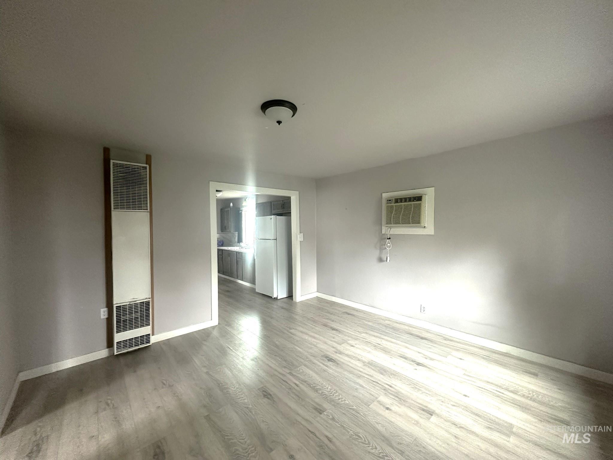Unfurnished bedroom with a heating unit, freestanding refrigerator, and light wood-style flooring