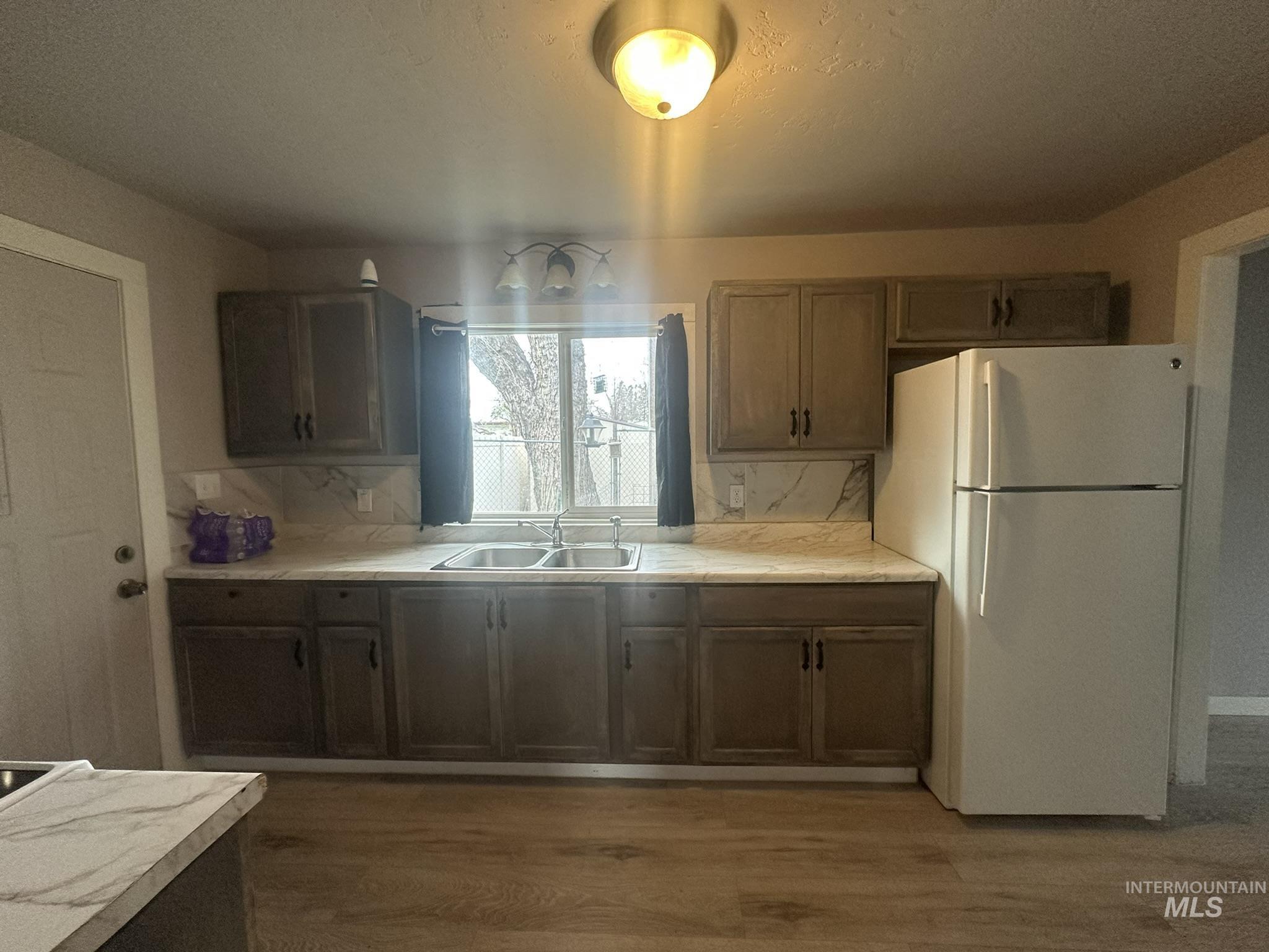 Kitchen featuring freestanding refrigerator, light countertops, dark wood-type flooring, backsplash, and a textured ceiling