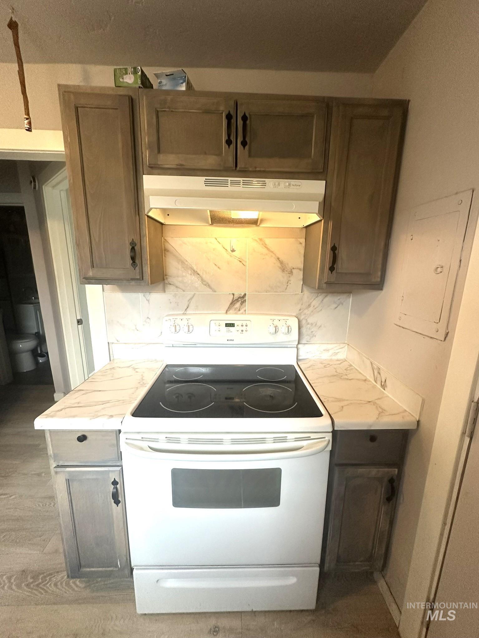 Kitchen with white range with electric cooktop, light countertops, electric panel, decorative backsplash, and dark wood finish cabinetry