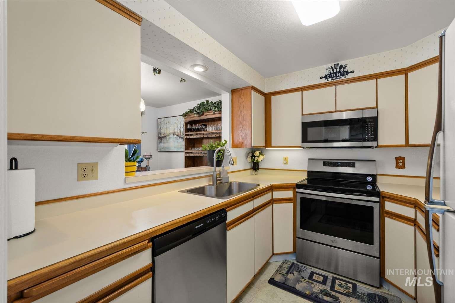 Kitchen with light countertops, appliances with stainless steel finishes, brown cabinets, a textured ceiling, and white cabinetry