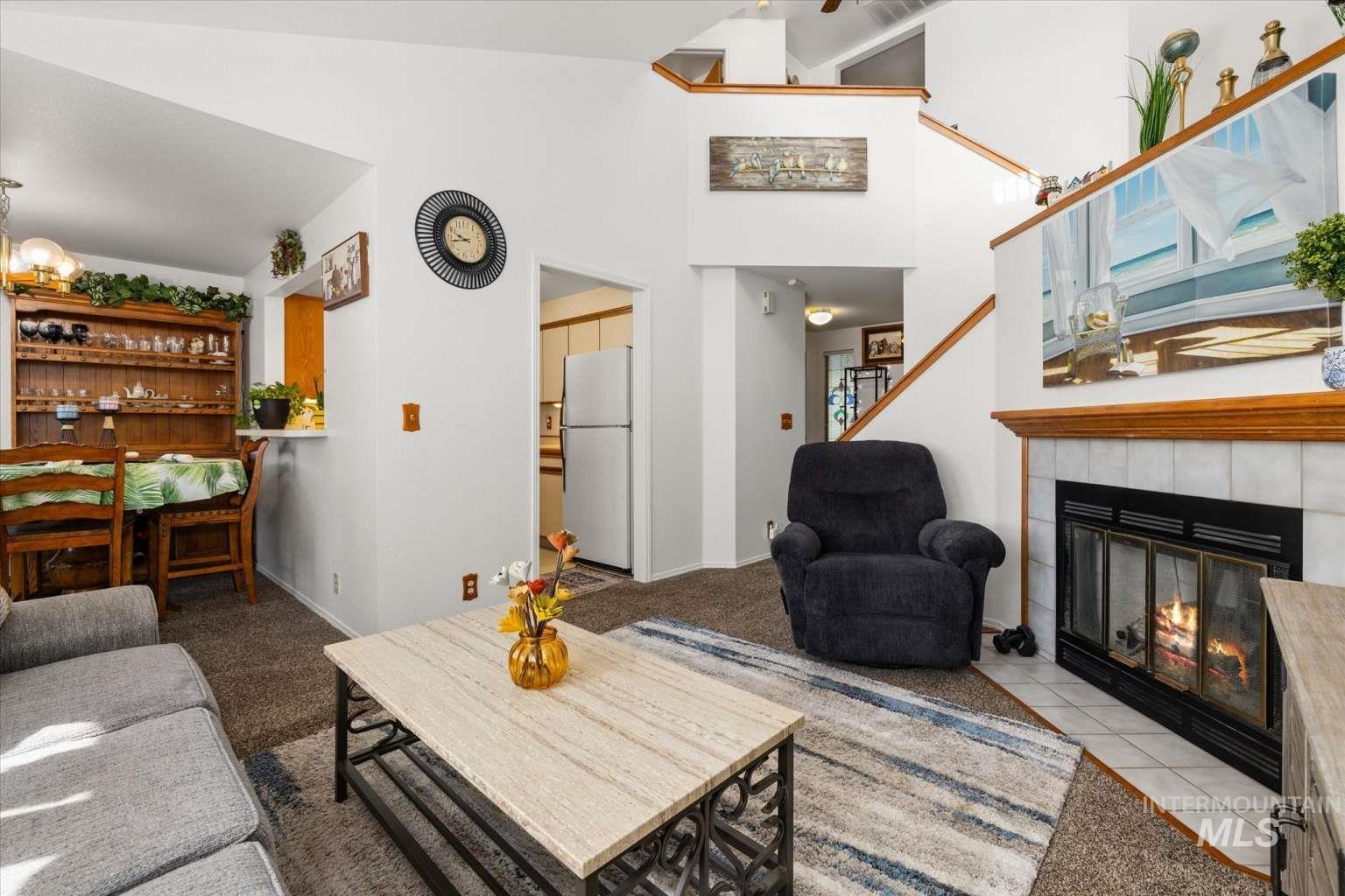 Living area with a chandelier, a tiled fireplace, carpet, high vaulted ceiling, and tile patterned flooring