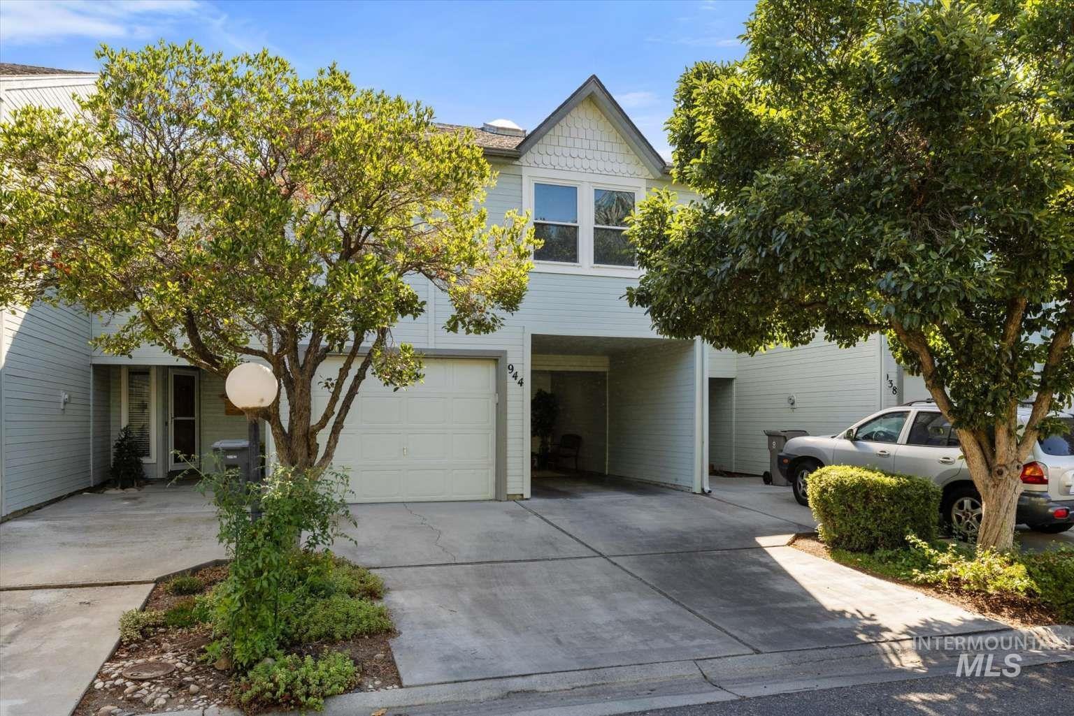 View of property hidden behind natural elements featuring an attached garage and concrete driveway