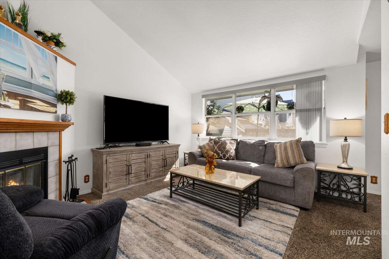 Living area featuring carpet floors, a tiled fireplace, and high vaulted ceiling