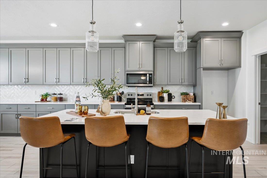 Kitchen featuring gray cabinets, a kitchen bar, light wood-type flooring, hanging light fixtures, and appliances with stainless steel finishes