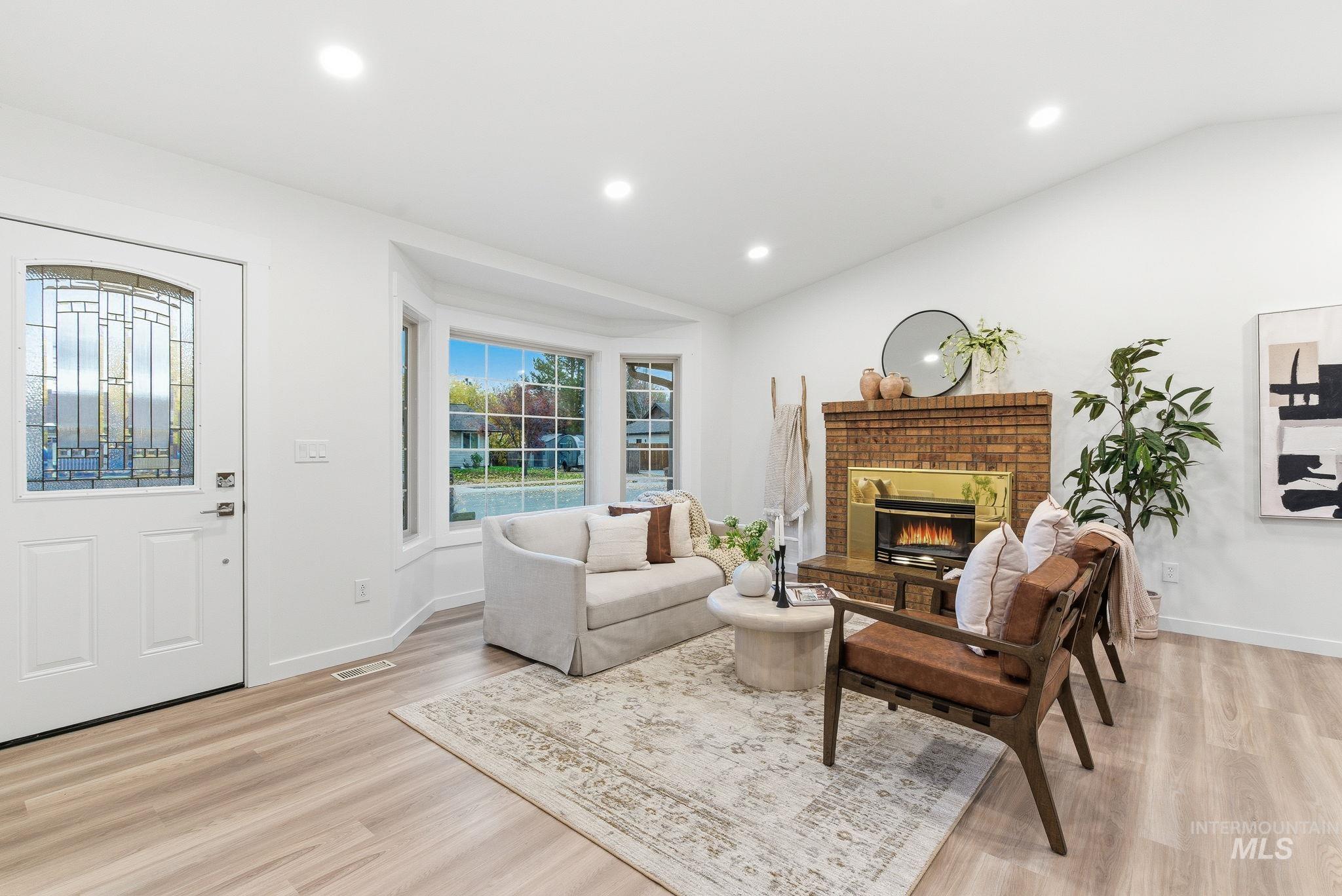 Living room with lofted ceiling, recessed lighting, a fireplace, and light wood-type flooring
