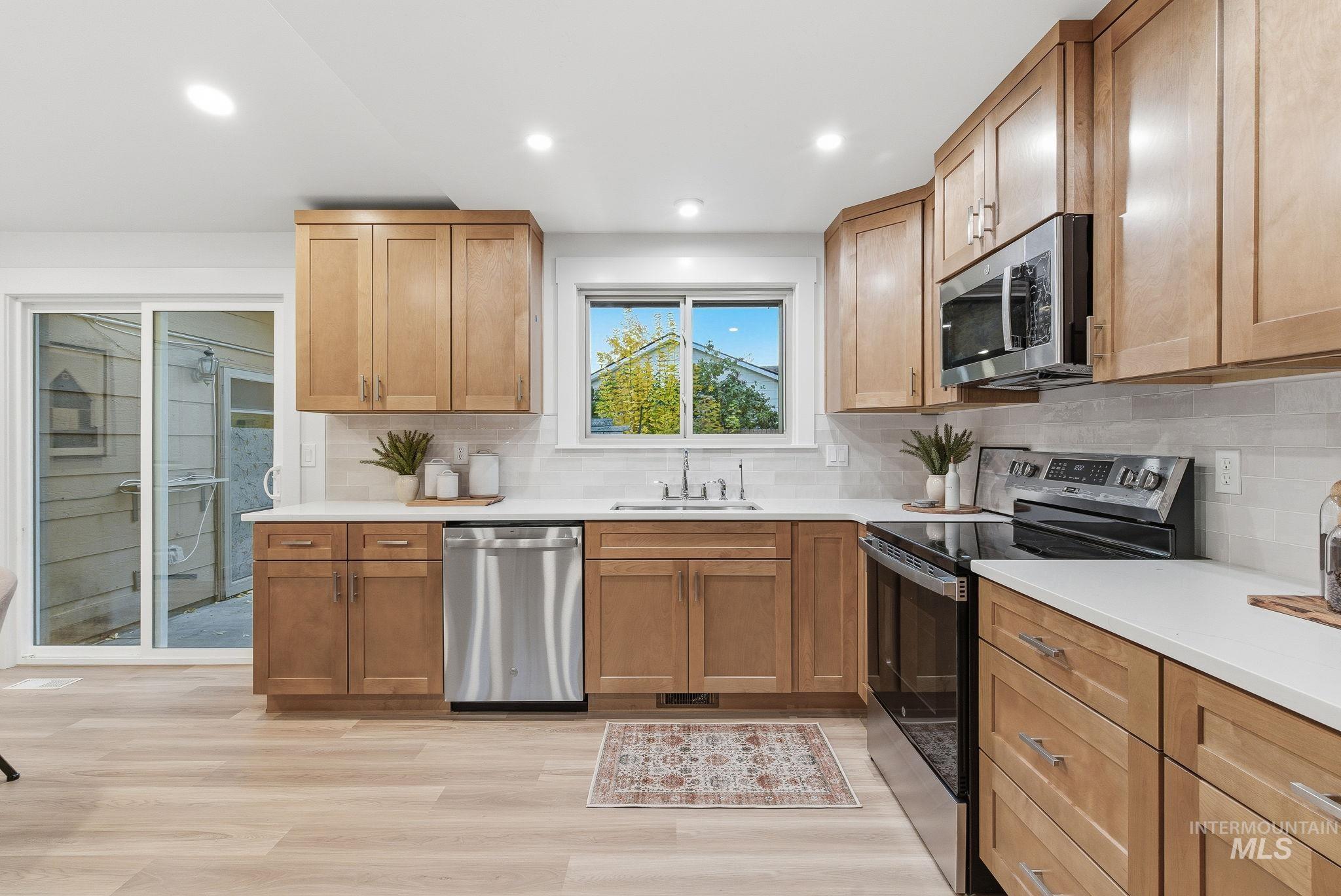 Kitchen with appliances with stainless steel finishes, tasteful backsplash, recessed lighting, light wood-type flooring, and light stone counters