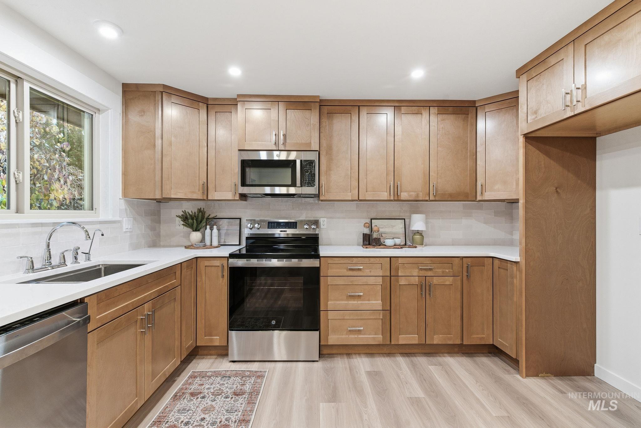 Kitchen featuring appliances with stainless steel finishes, backsplash, light wood-style floors, brown cabinets, and light stone counters