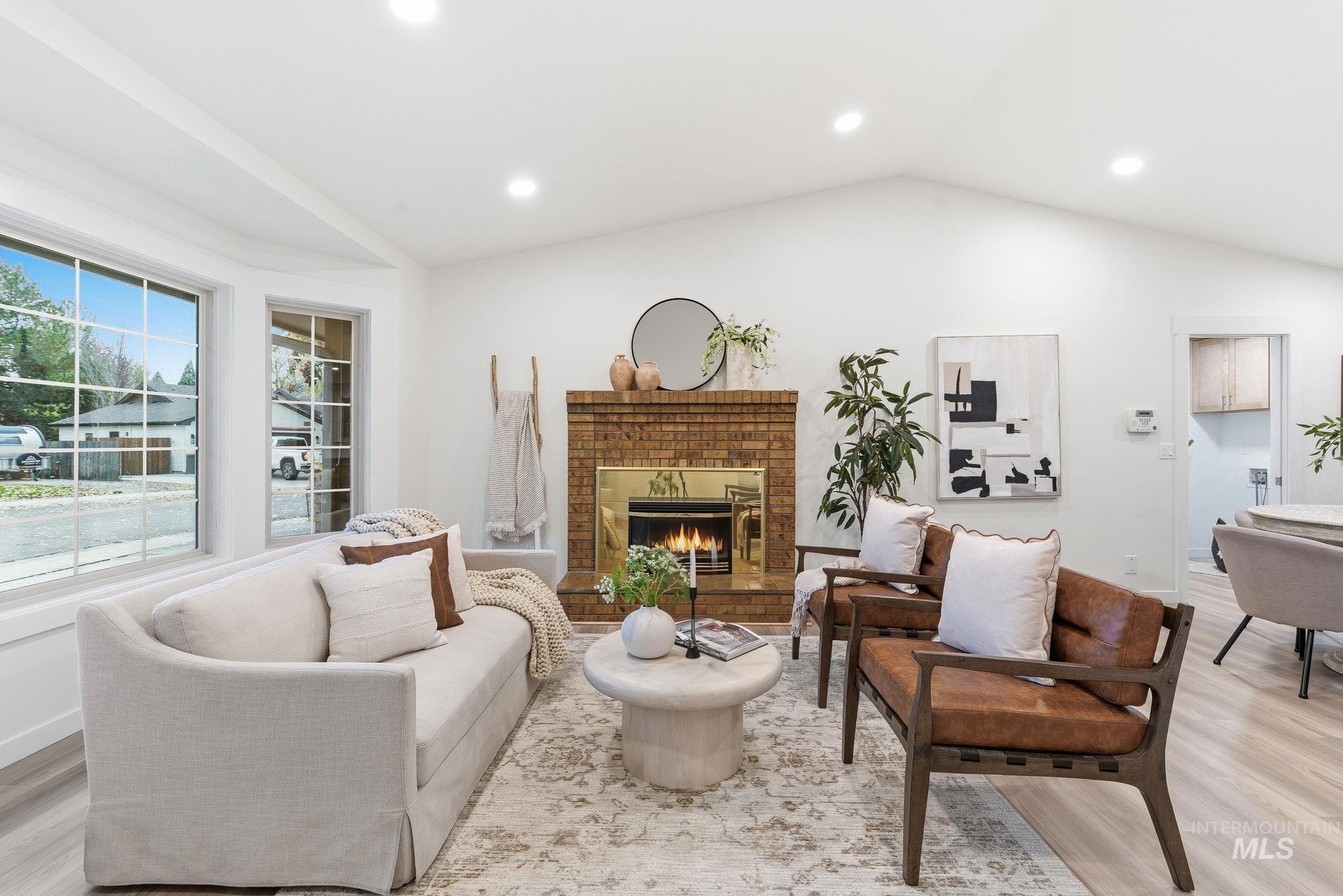 Living room featuring light wood finished floors, vaulted ceiling, a brick fireplace, and recessed lighting