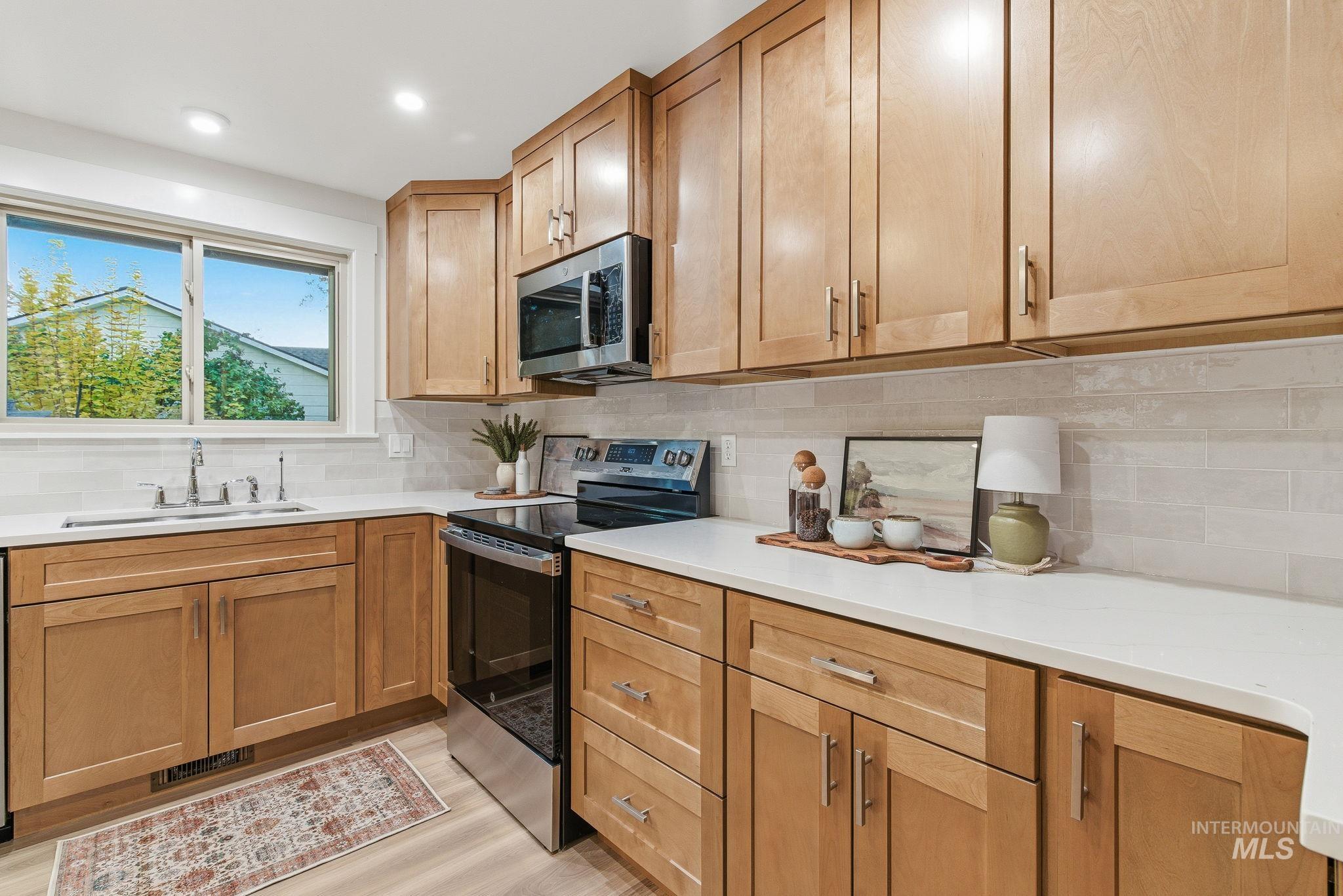 Kitchen featuring stainless steel appliances, decorative backsplash, light wood-type flooring, light stone counters, and recessed lighting
