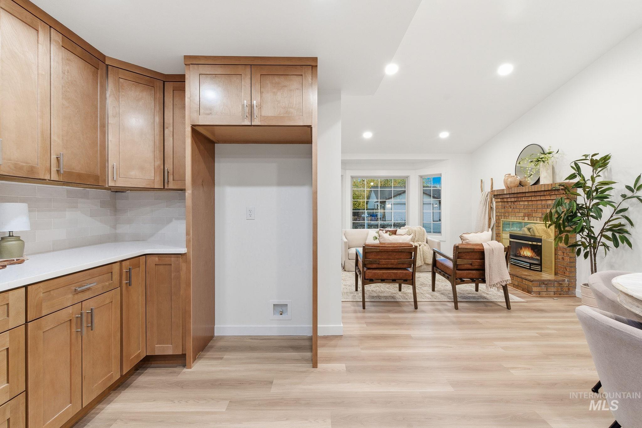 Kitchen featuring brown cabinetry, light wood-style floors, recessed lighting, decorative backsplash, and a brick fireplace