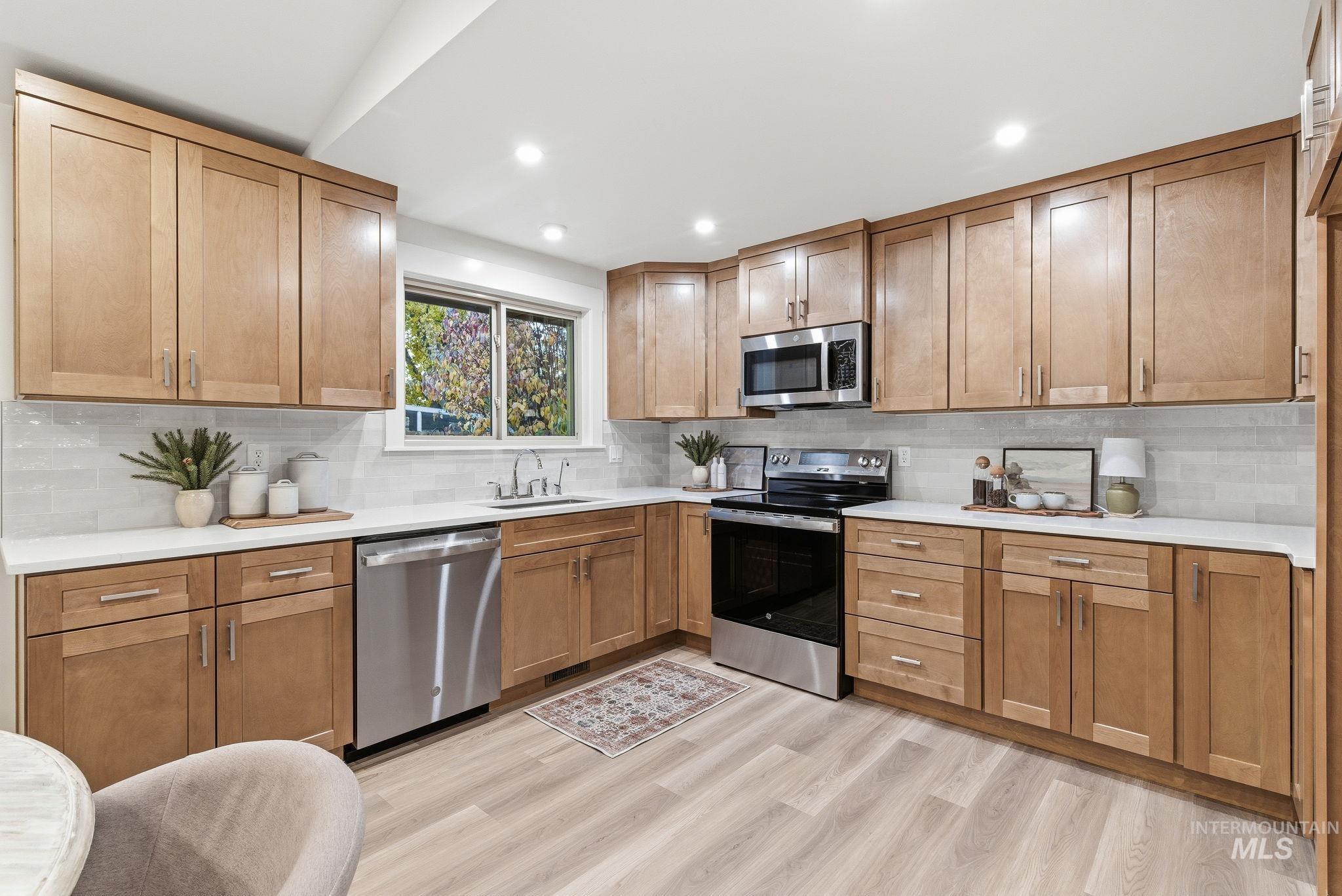 Kitchen with appliances with stainless steel finishes, backsplash, recessed lighting, brown cabinetry, and light wood-style flooring