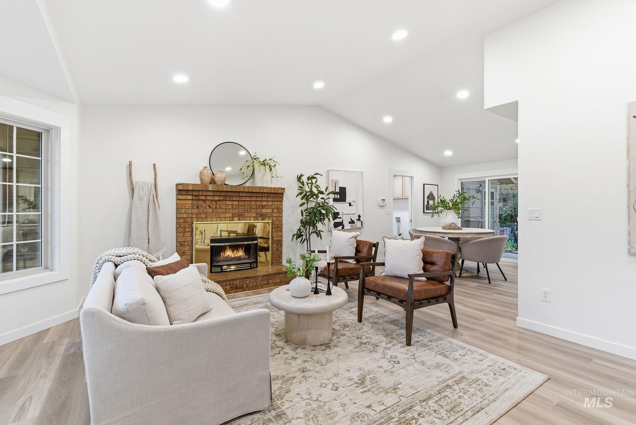 Living area featuring lofted ceiling, light wood finished floors, a brick fireplace, and recessed lighting