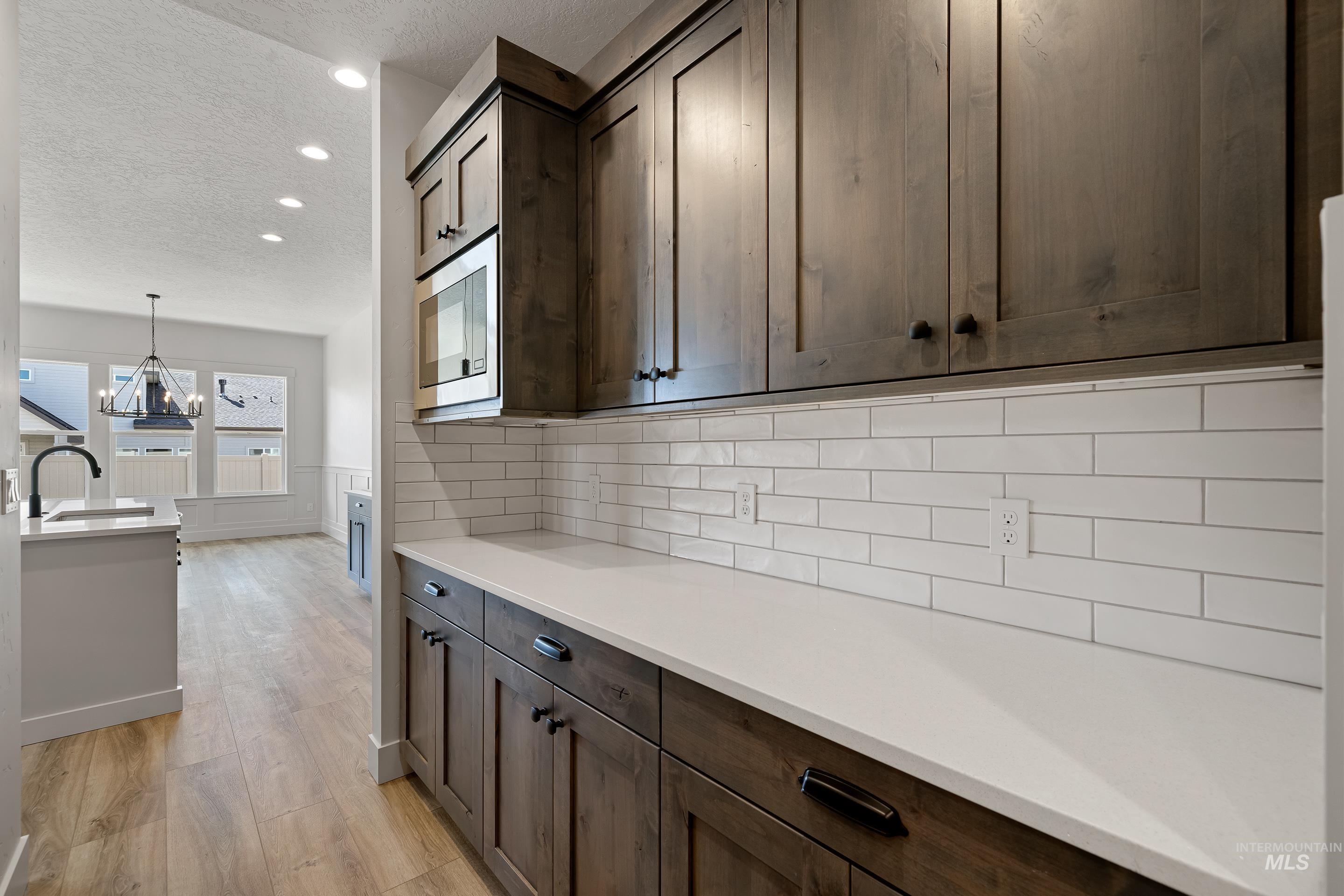 Kitchen with a textured ceiling, a chandelier, light wood finished floors, recessed lighting, and dark brown cabinets