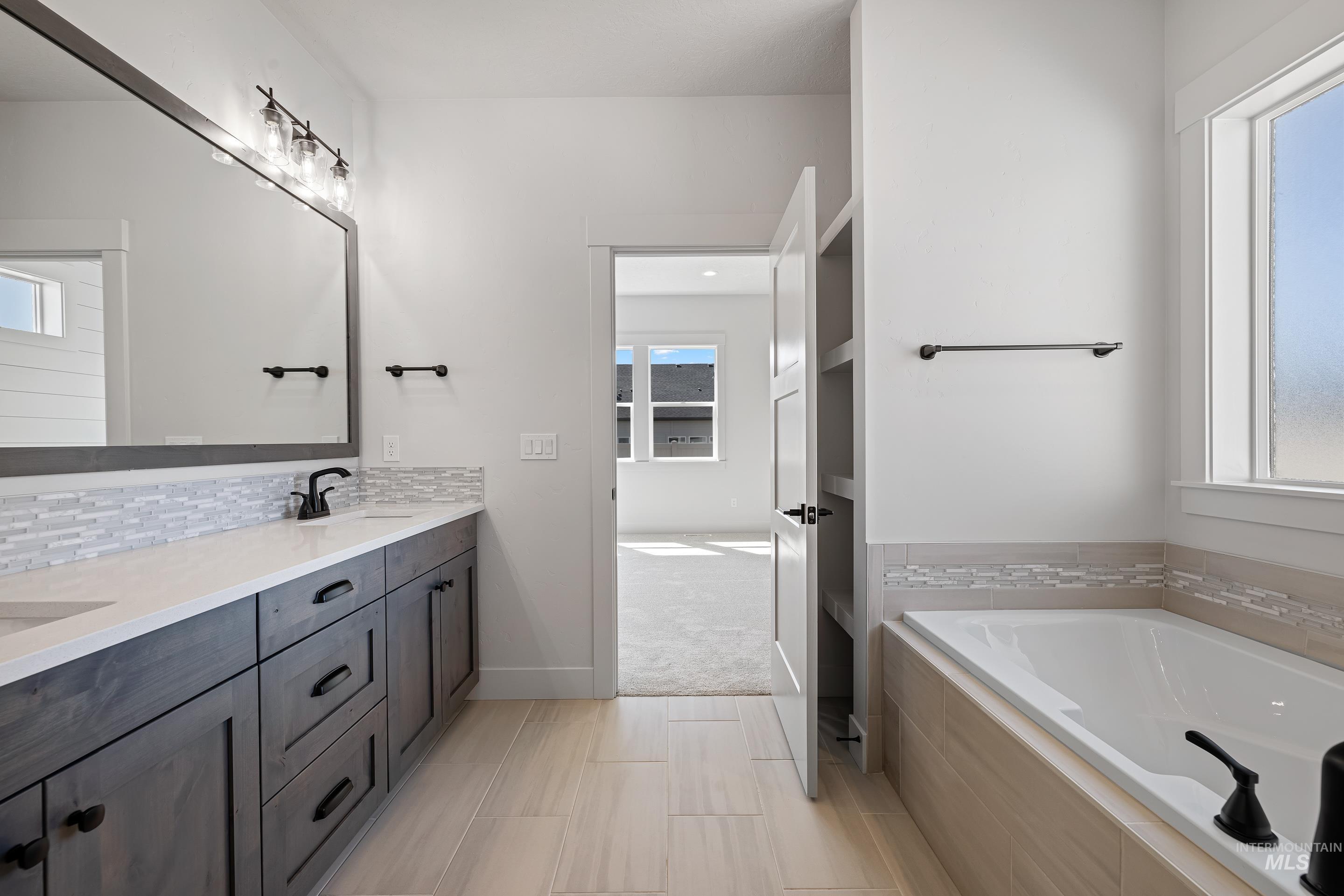 Full bath with healthy amount of natural light, a bath, double vanity, and backsplash