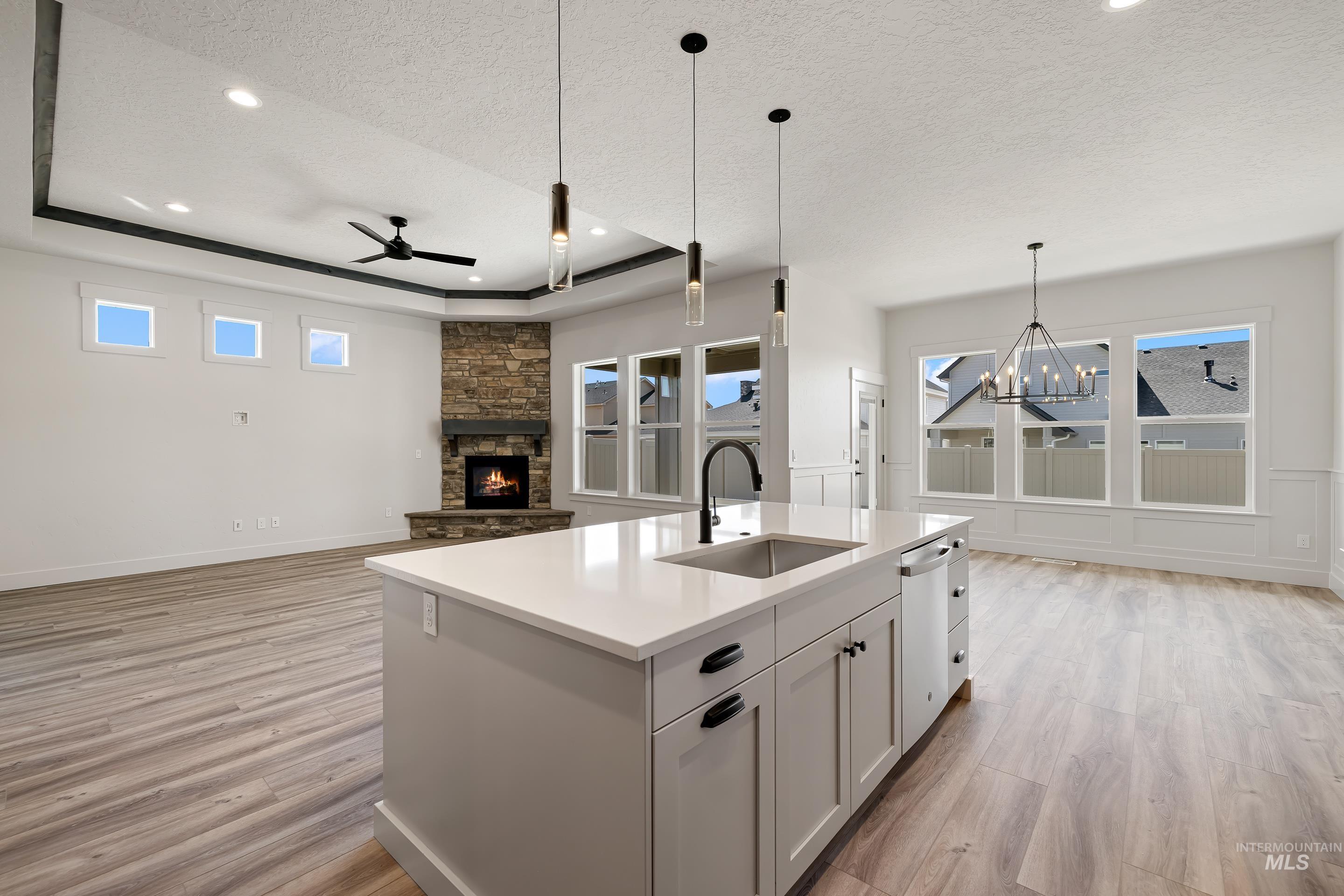 Kitchen with open floor plan, a tray ceiling, a stone fireplace, white cabinetry, and decorative light fixtures