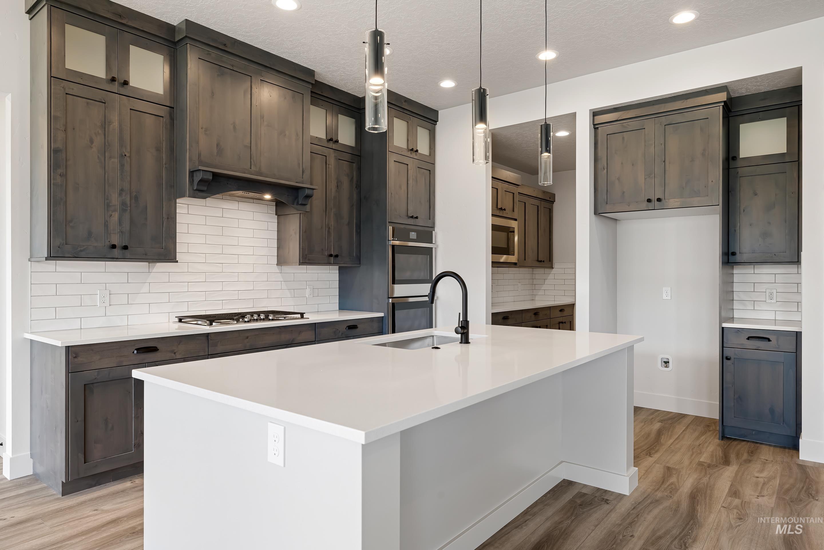 Kitchen with decorative backsplash, light wood-type flooring, glass insert cabinets, a center island with sink, and a textured ceiling