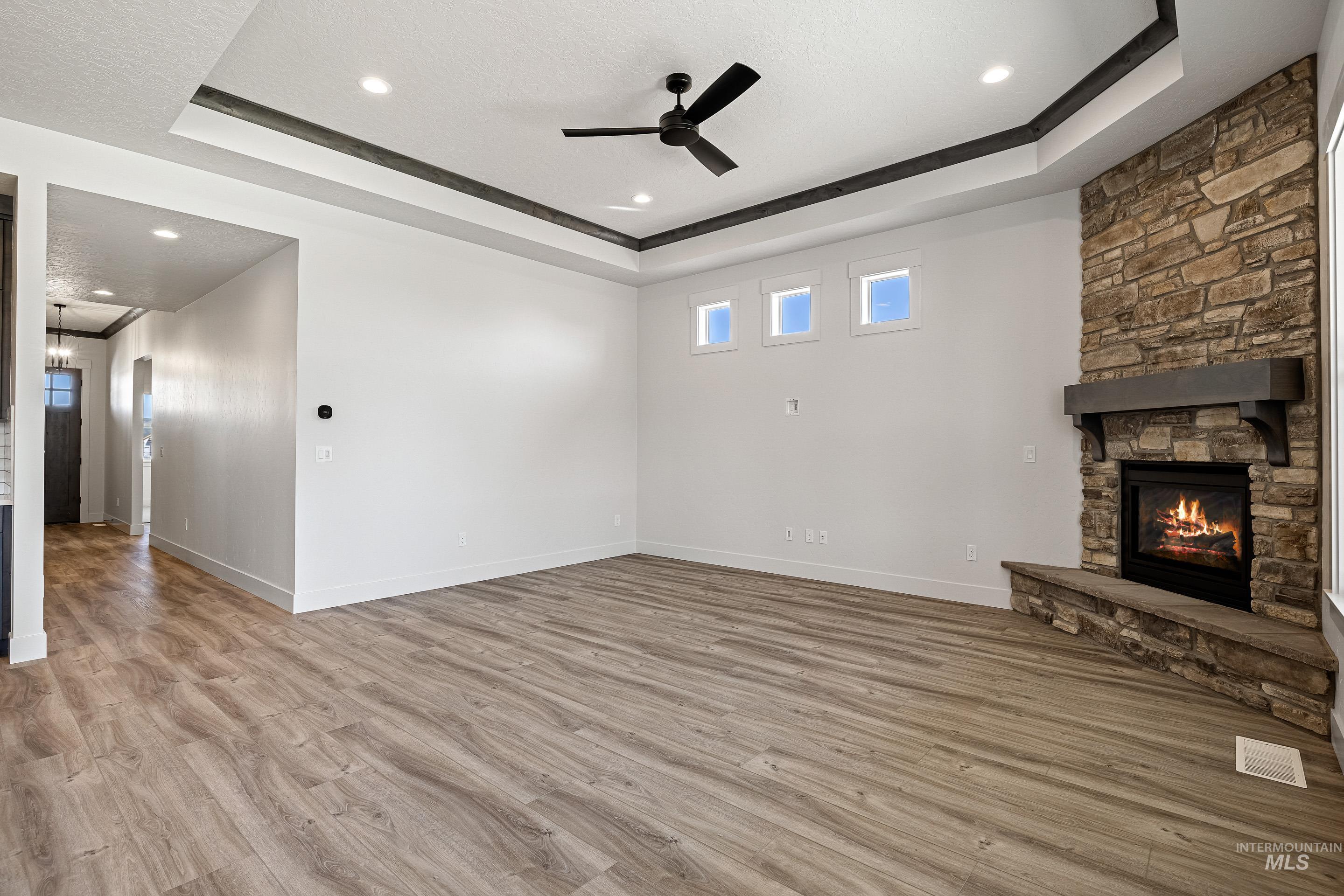 Unfurnished living room featuring a tray ceiling, light wood-style flooring, a ceiling fan, a fireplace, and recessed lighting