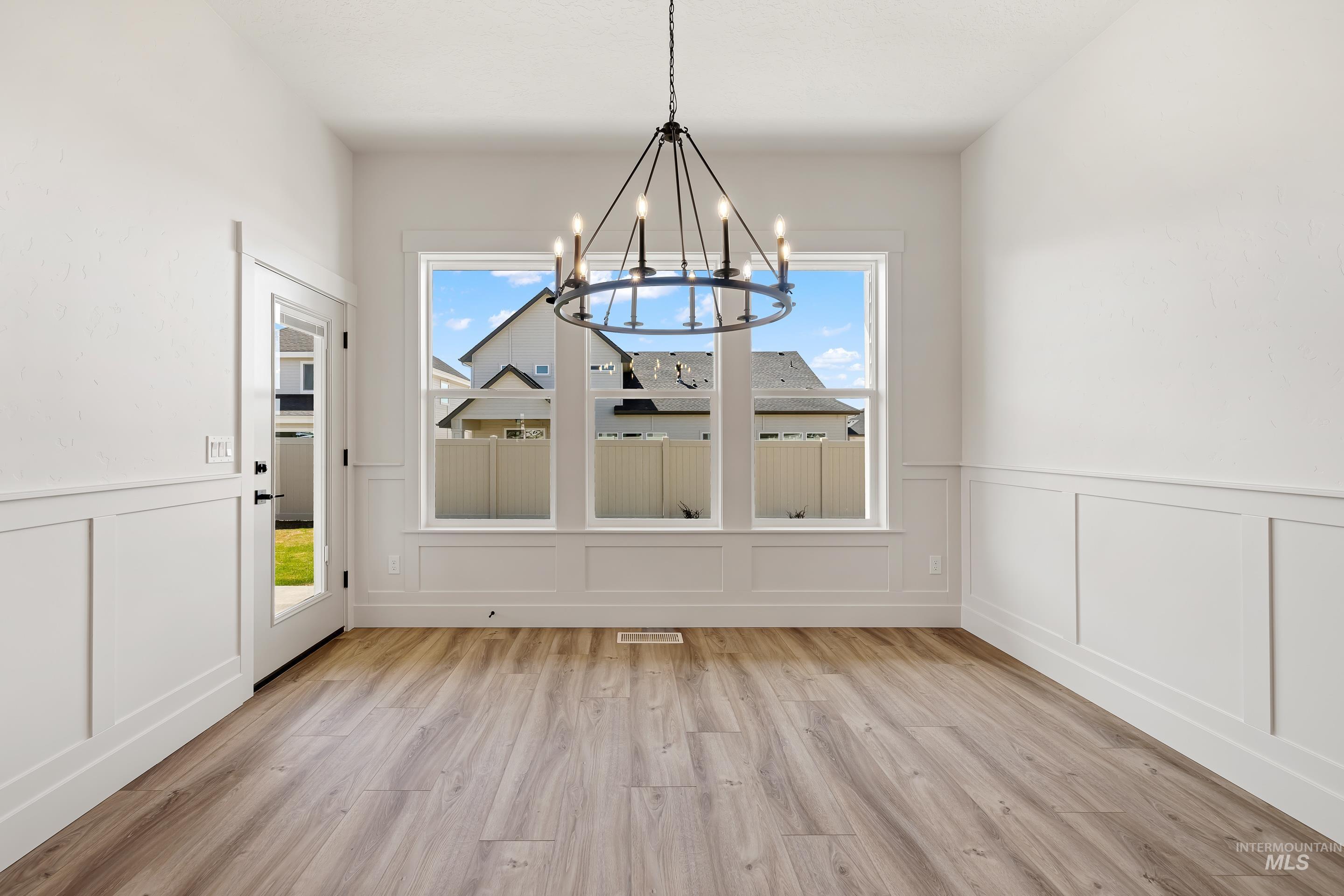 Unfurnished dining area featuring a decorative wall, wainscoting, healthy amount of natural light, light wood-type flooring, and a chandelier