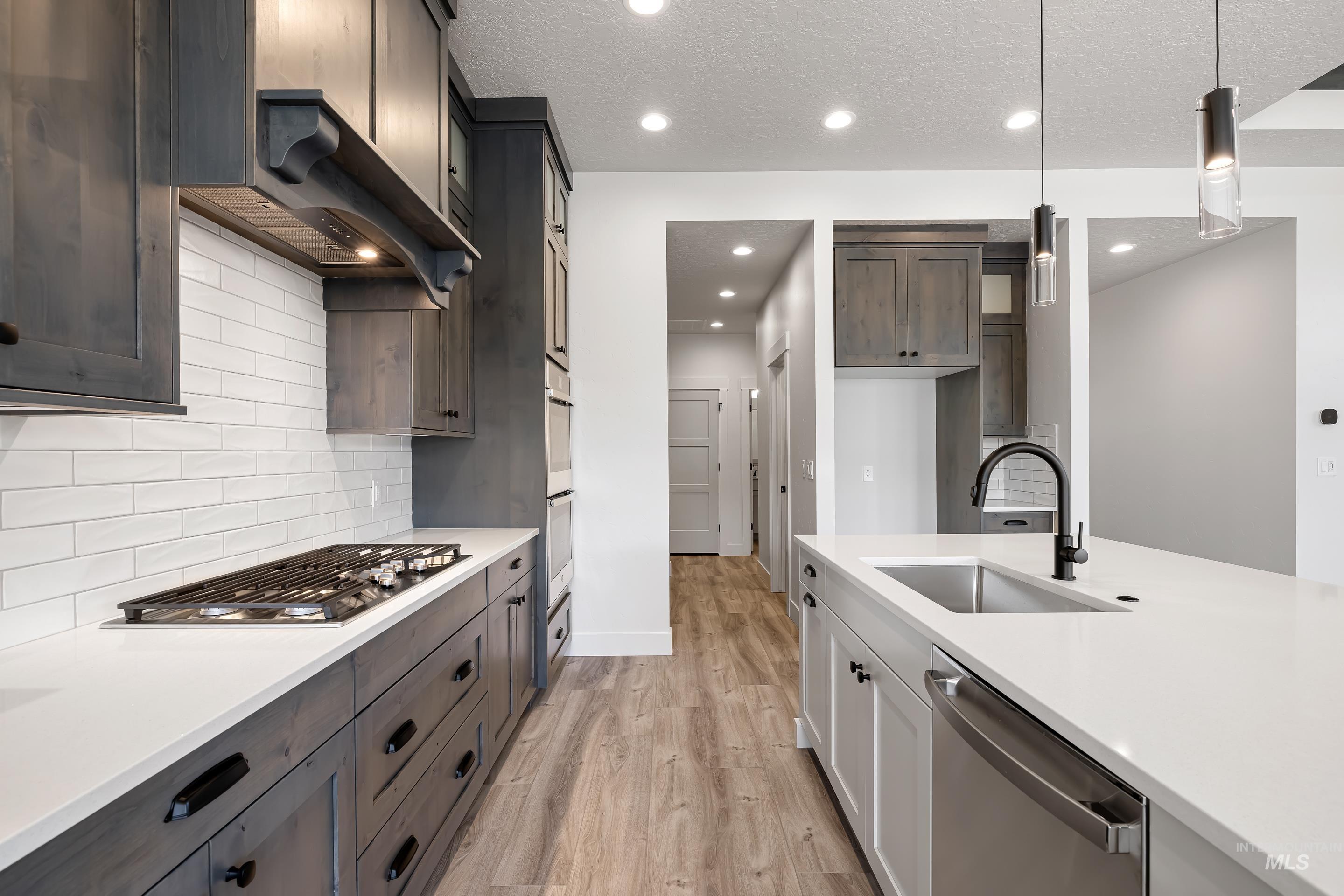 Kitchen with appliances with stainless steel finishes, light stone counters, light wood-style flooring, recessed lighting, and a textured ceiling