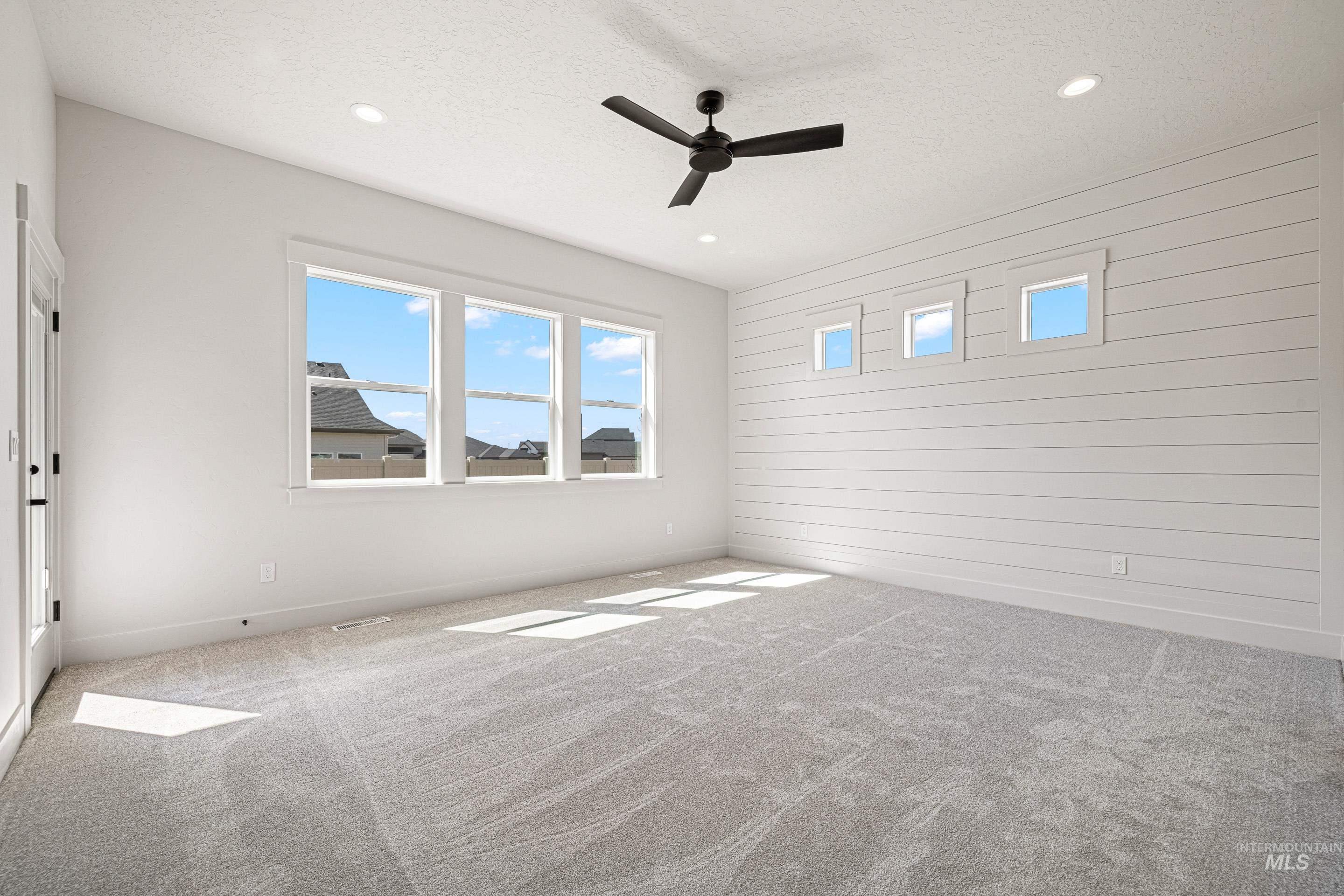 Carpeted empty room featuring plenty of natural light, a textured ceiling, ceiling fan, recessed lighting, and wooden walls