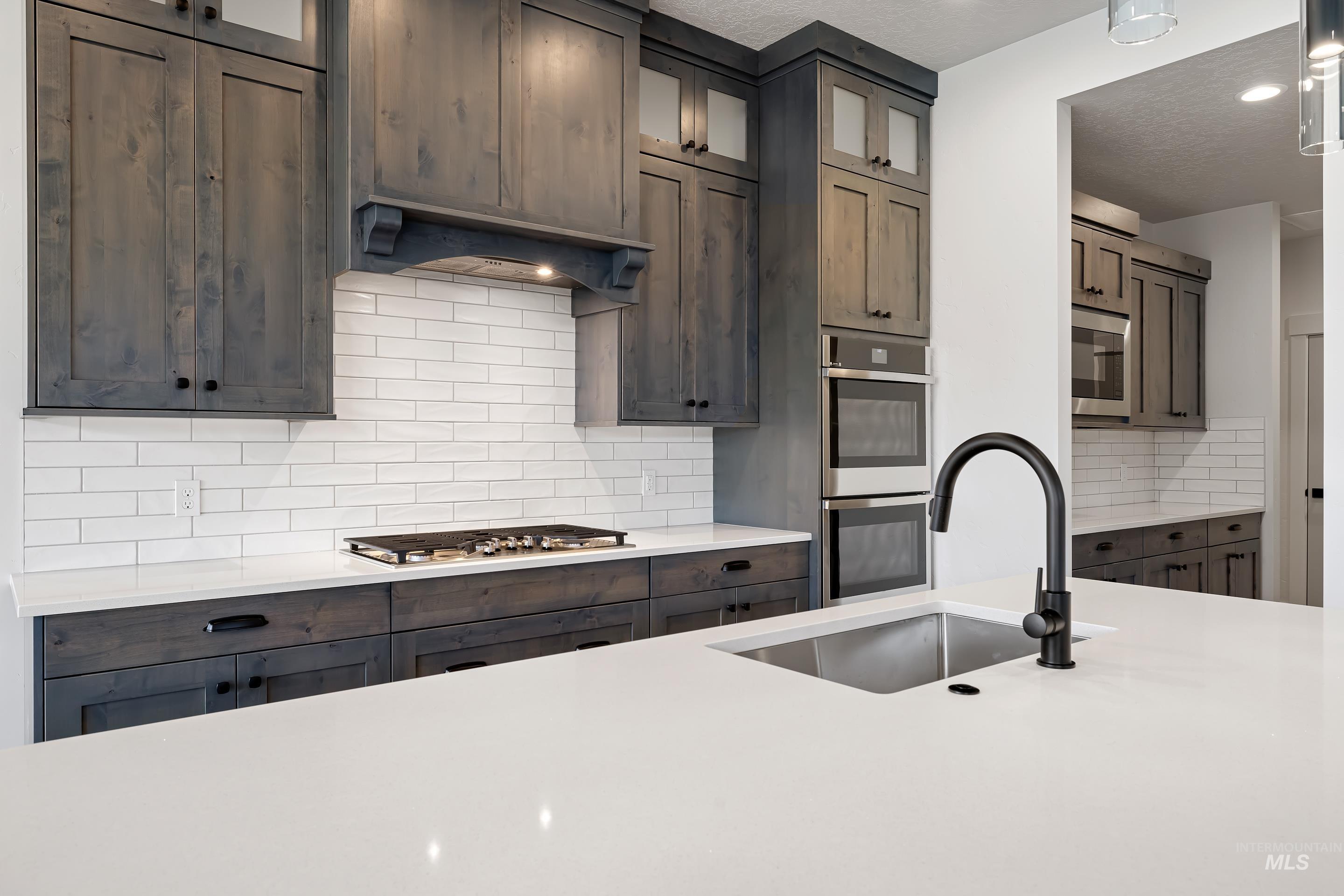 Kitchen featuring backsplash, glass insert cabinets, appliances with stainless steel finishes, light stone countertops, and a textured ceiling