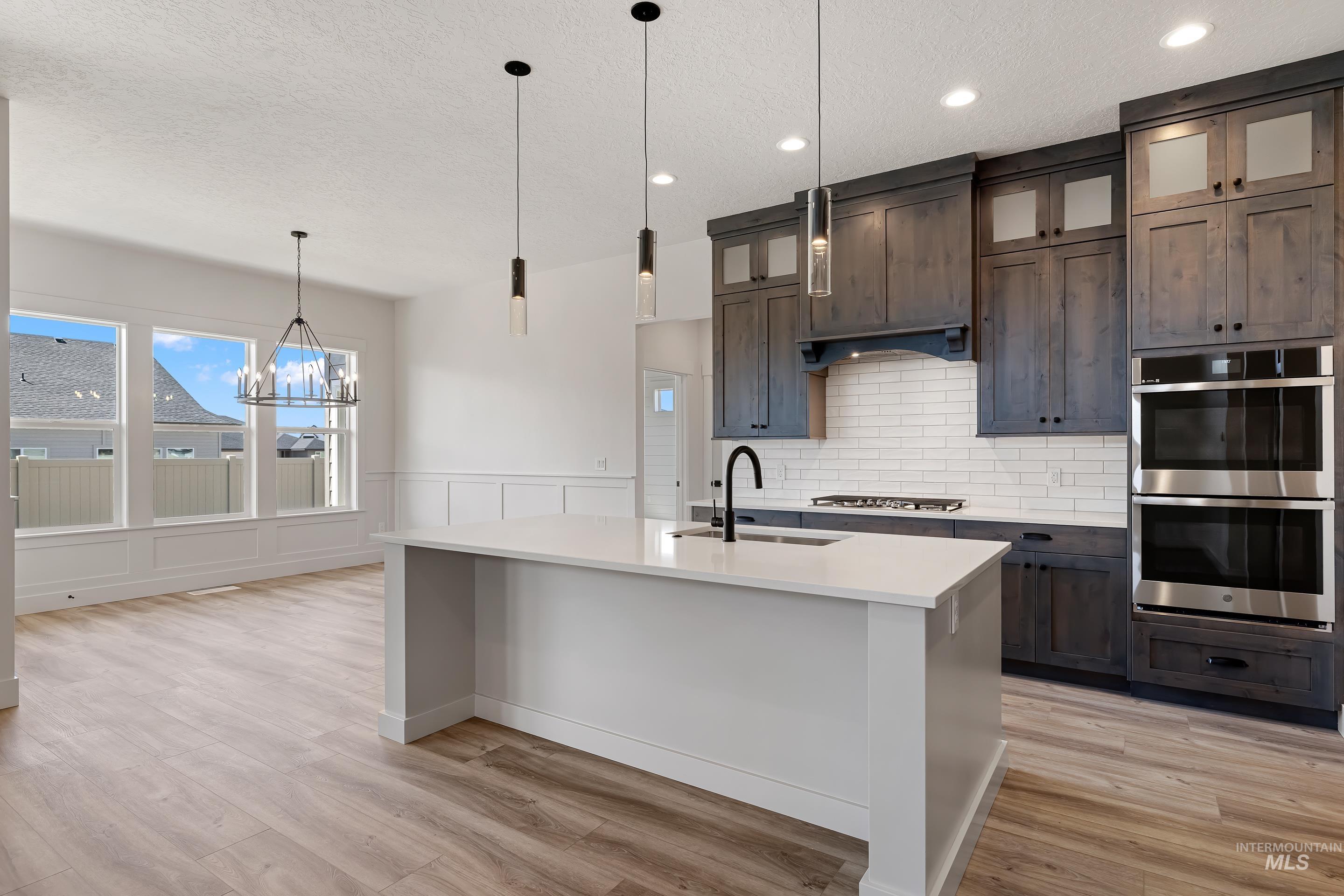 Kitchen with backsplash, hanging light fixtures, double oven, glass insert cabinets, and light wood-style flooring