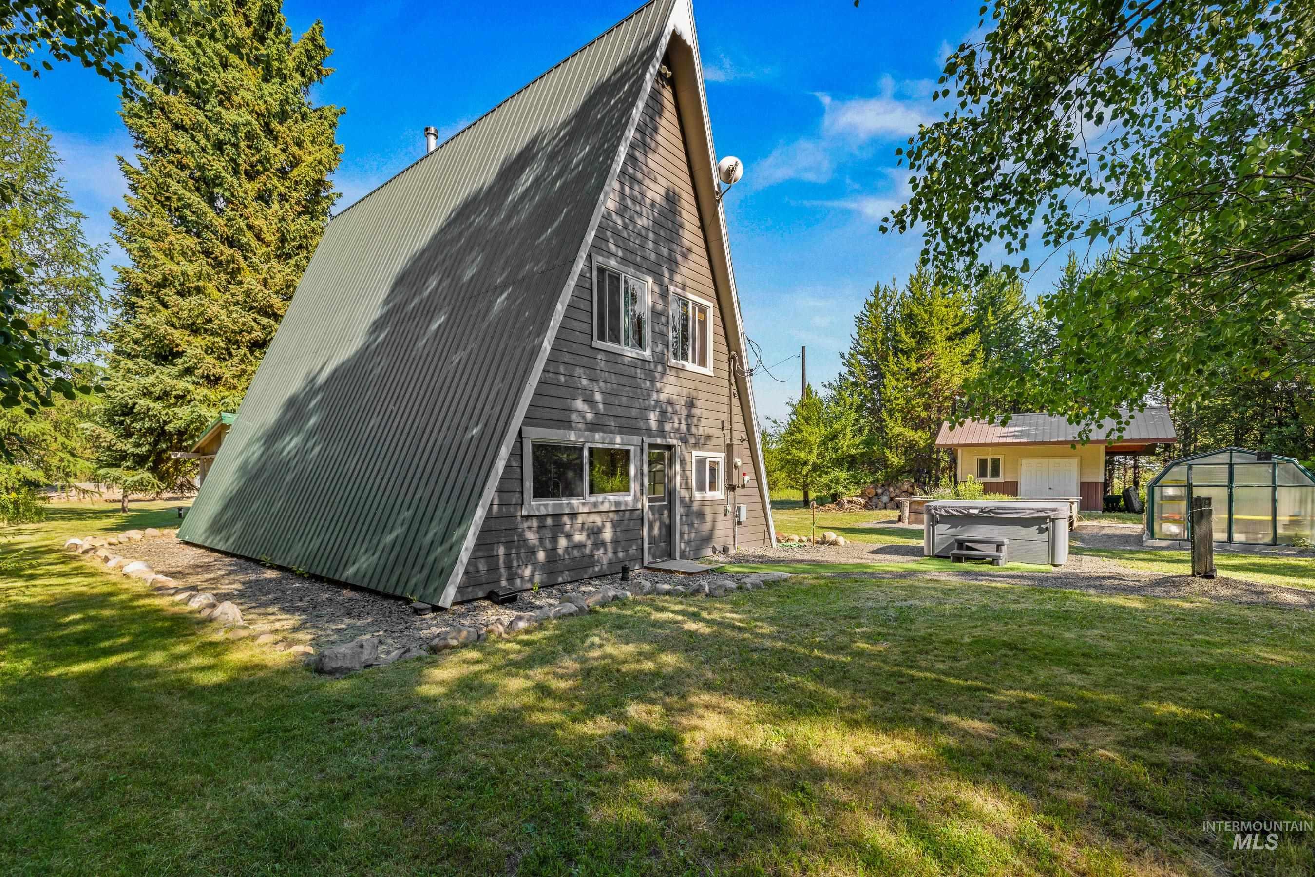Rear view of house featuring an outdoor structure, a lawn, a greenhouse, and a metal roof