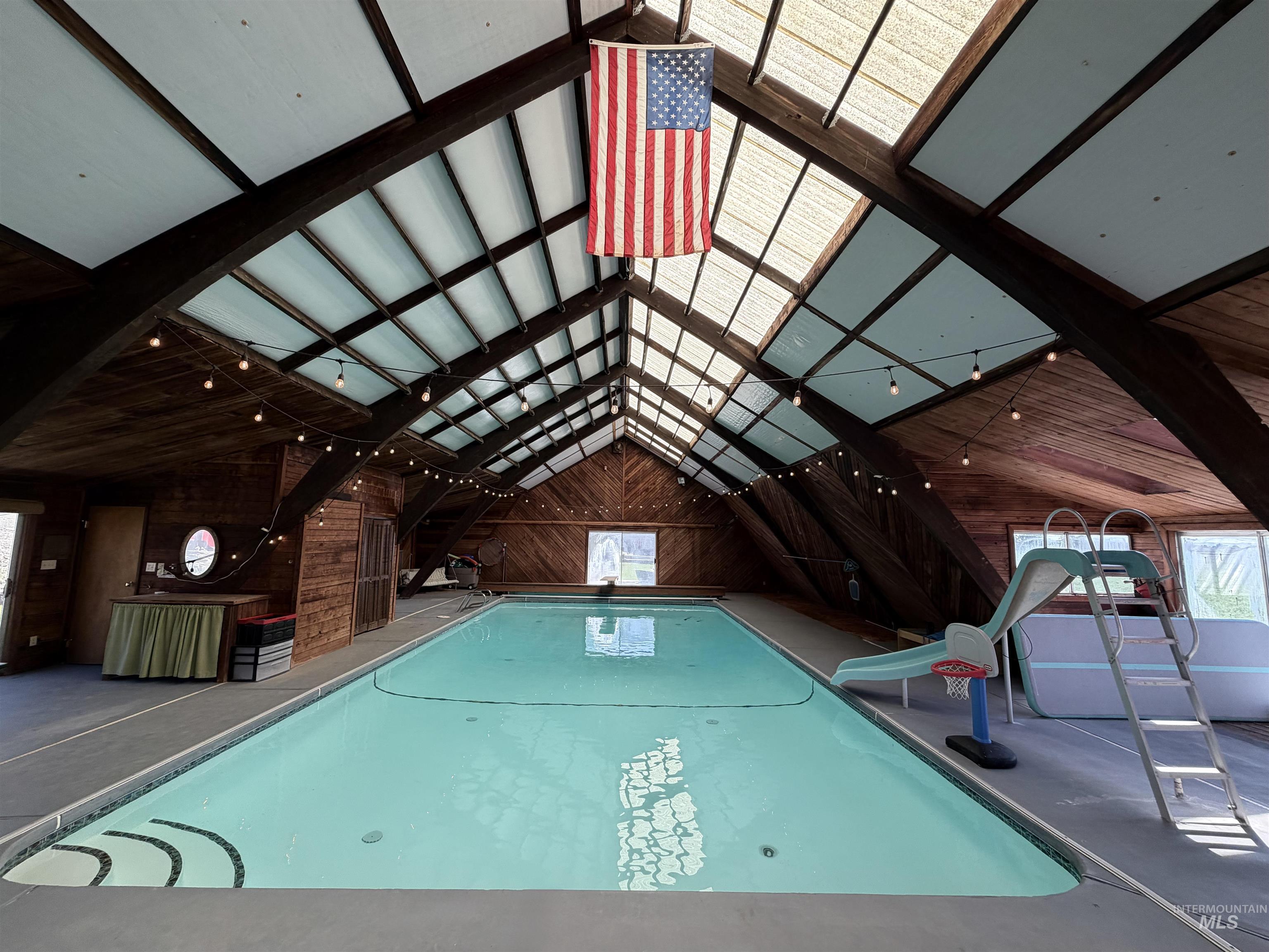 Indoor swimming pool featuring an A-frame ceiling with exposed dark wood beams and skylights