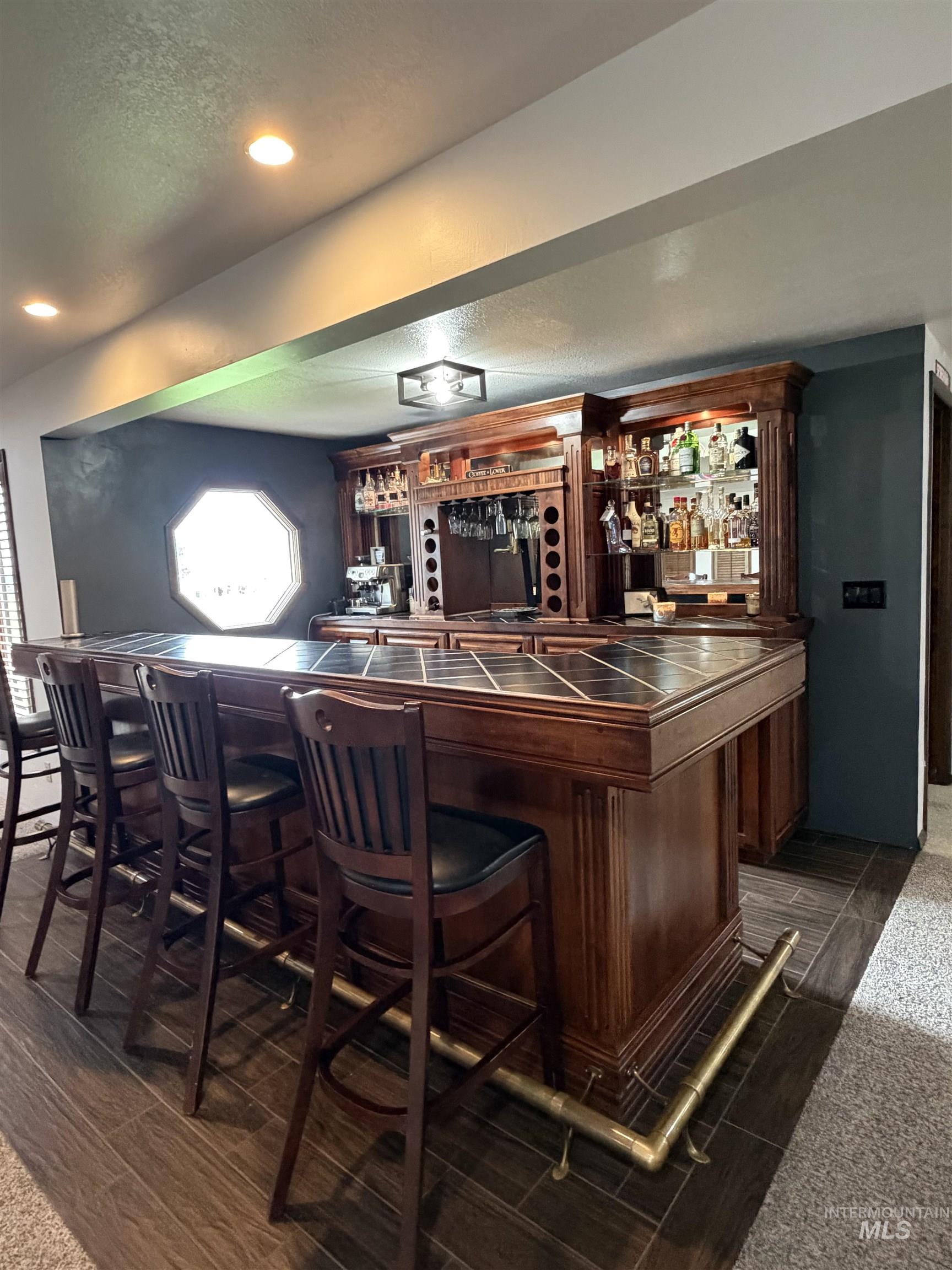 Custom built-in bar featuring wood-finish cabinetry, a tile countertop, and integrated shelving