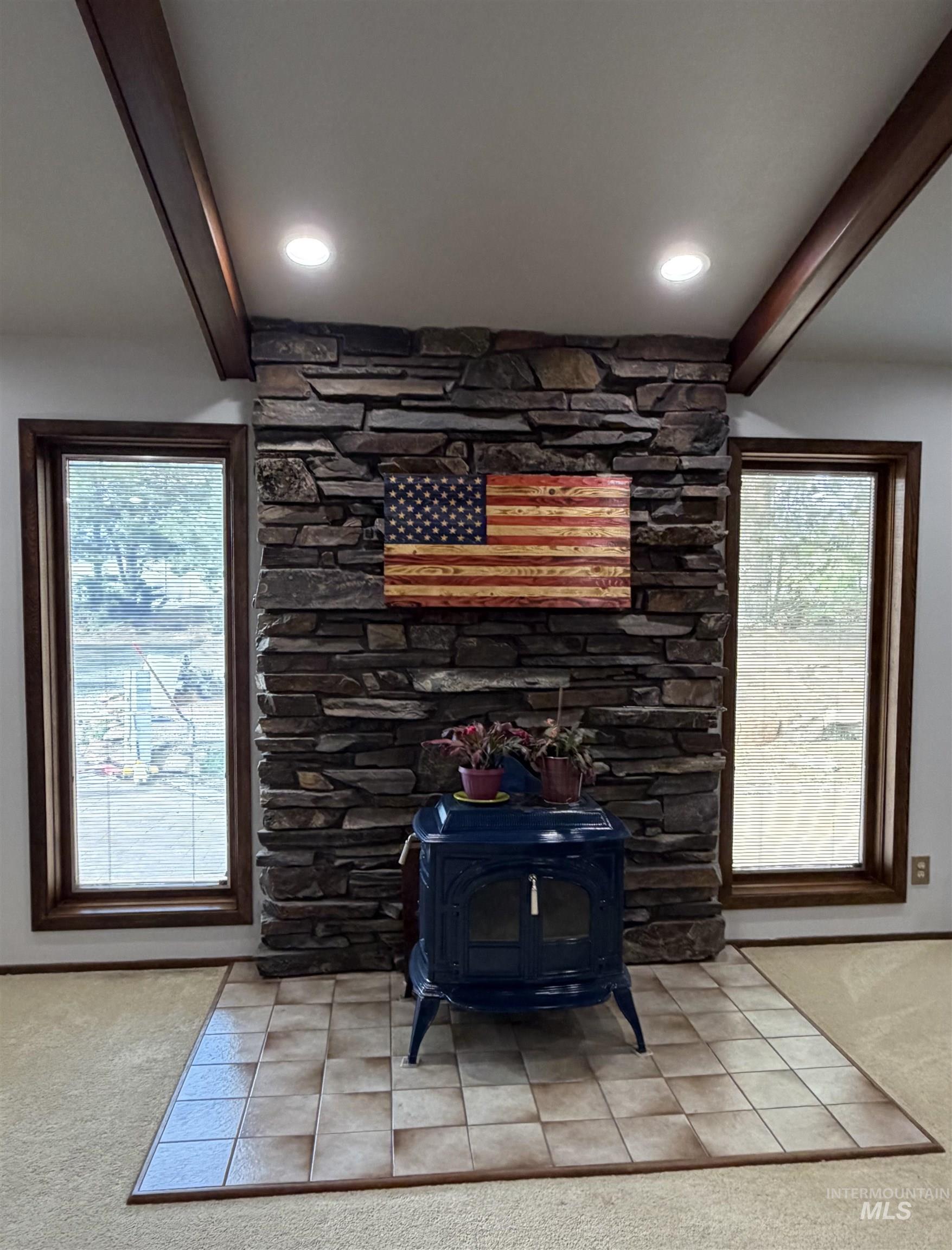 Stacked stone fireplace with a blue wood-burning stove, framed by two vertical windows with dark wood trim