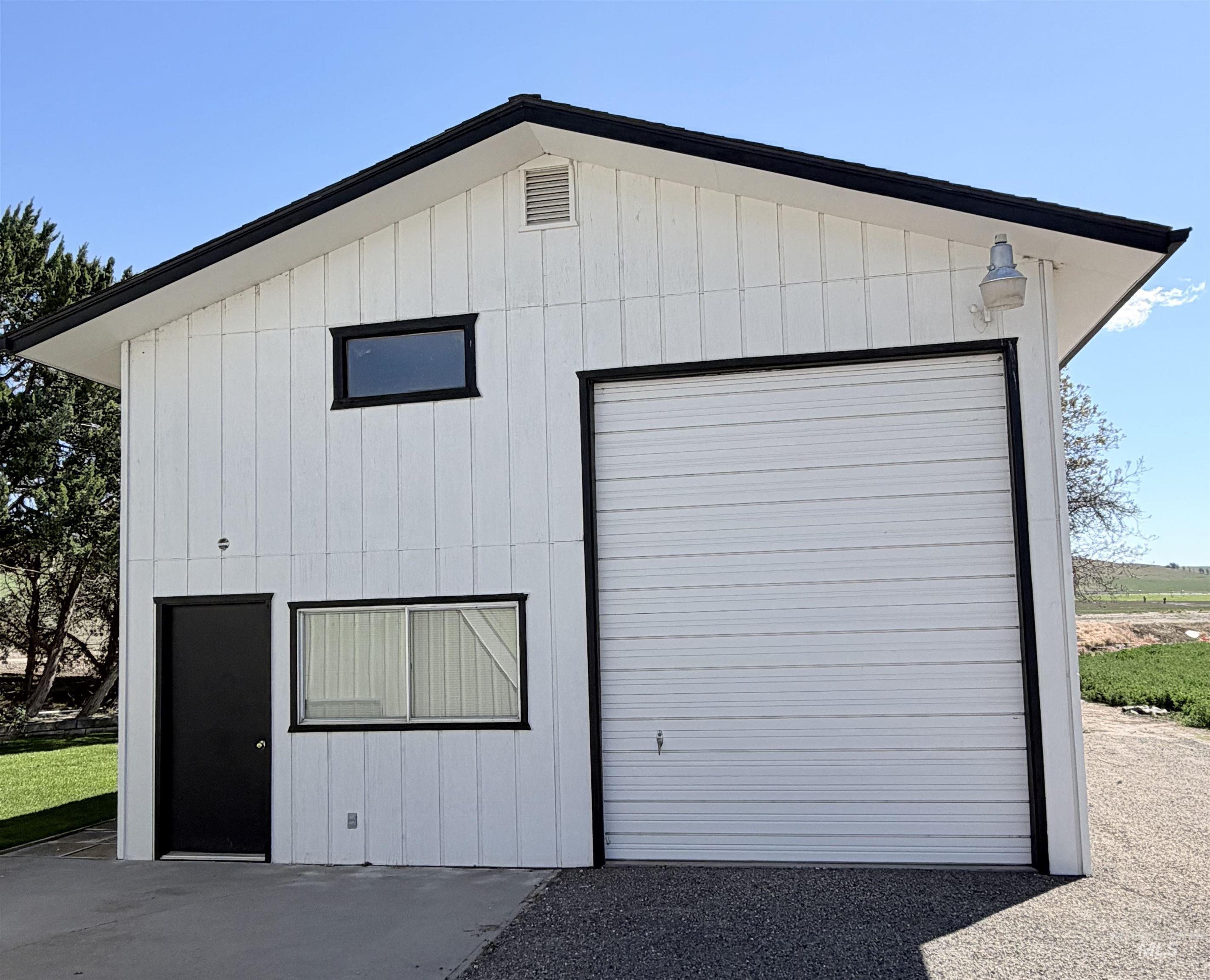 Two-story white vertical siding structure featuring a large garage door with black trim, a black entry door, and multiple windows