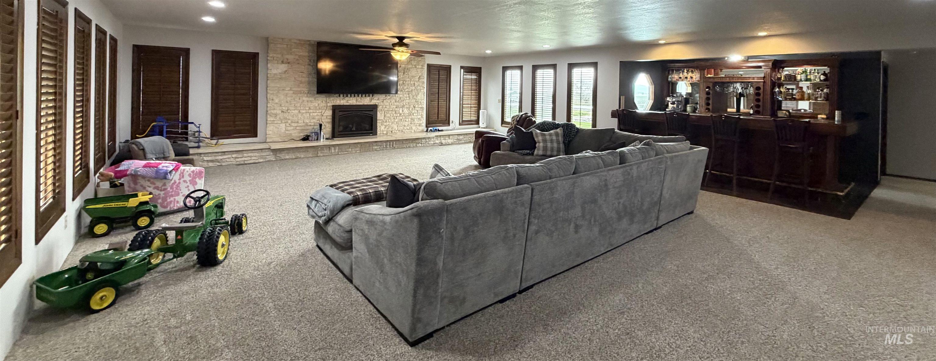 Spacious entertainment area featuring recessed lighting, a stone-clad fireplace, and a full-service wet bar