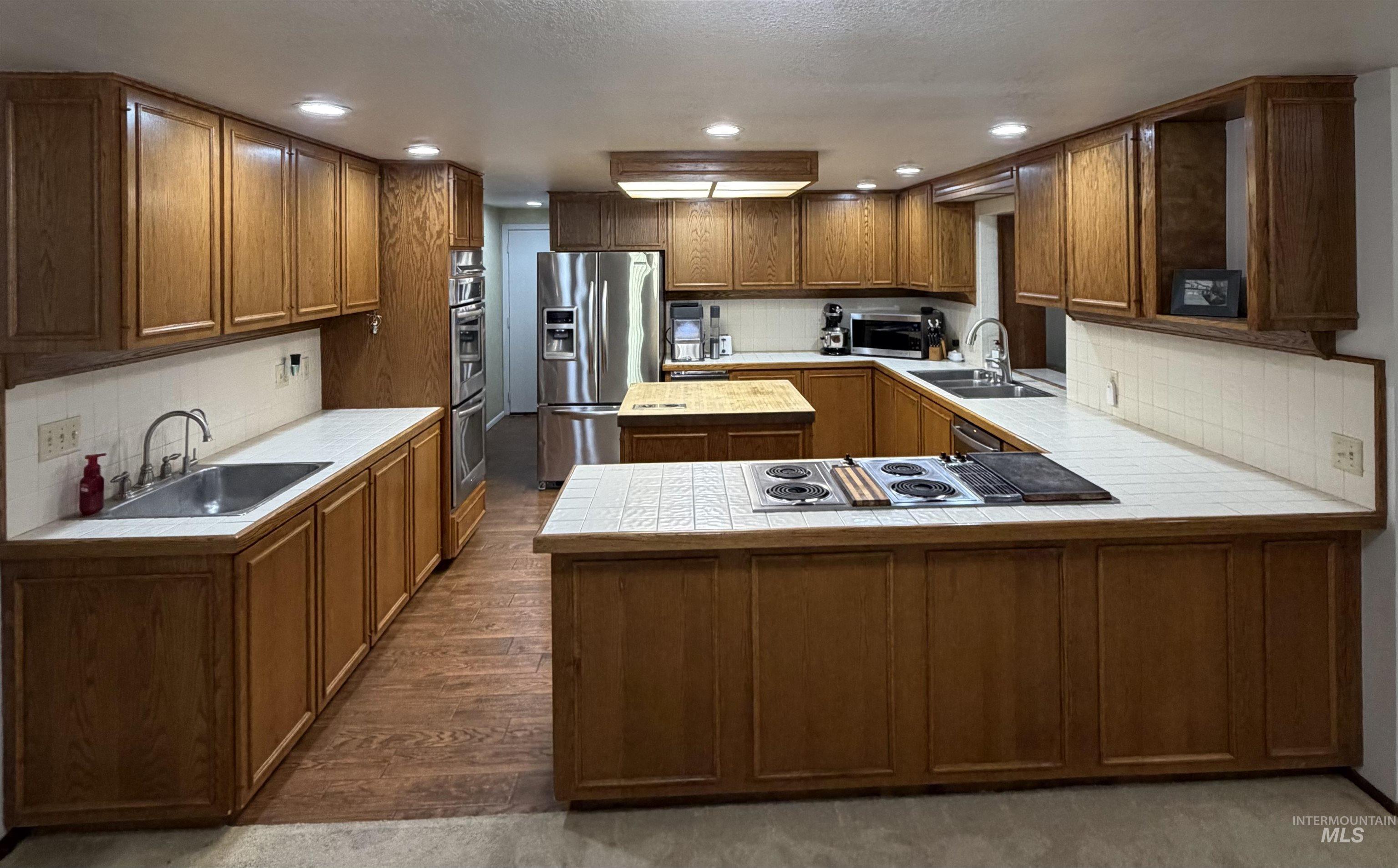 Kitchen featuring ample wood cabinetry, white tile countertops, and integrated stainless steel appliances