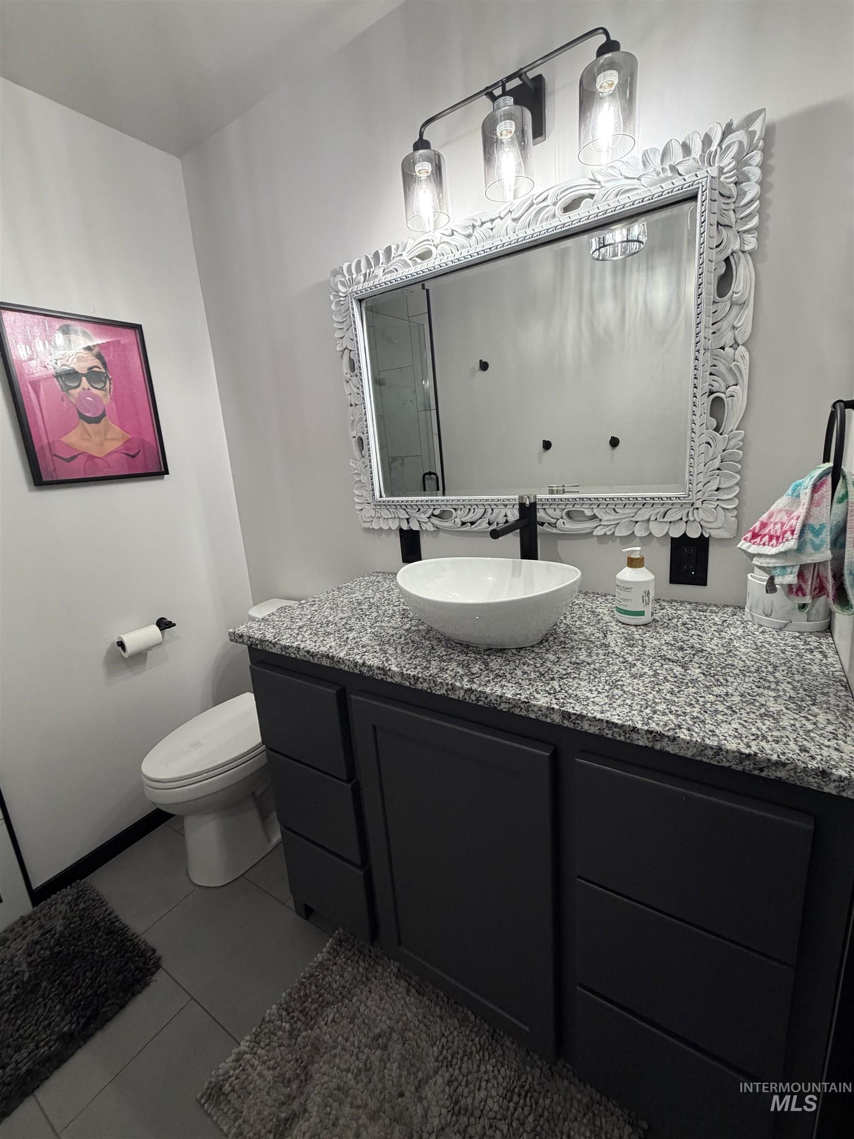 Bathroom vanity featuring a vessel sink, dark cabinetry with ample storage, a granite countertop, and an ornate framed mirror