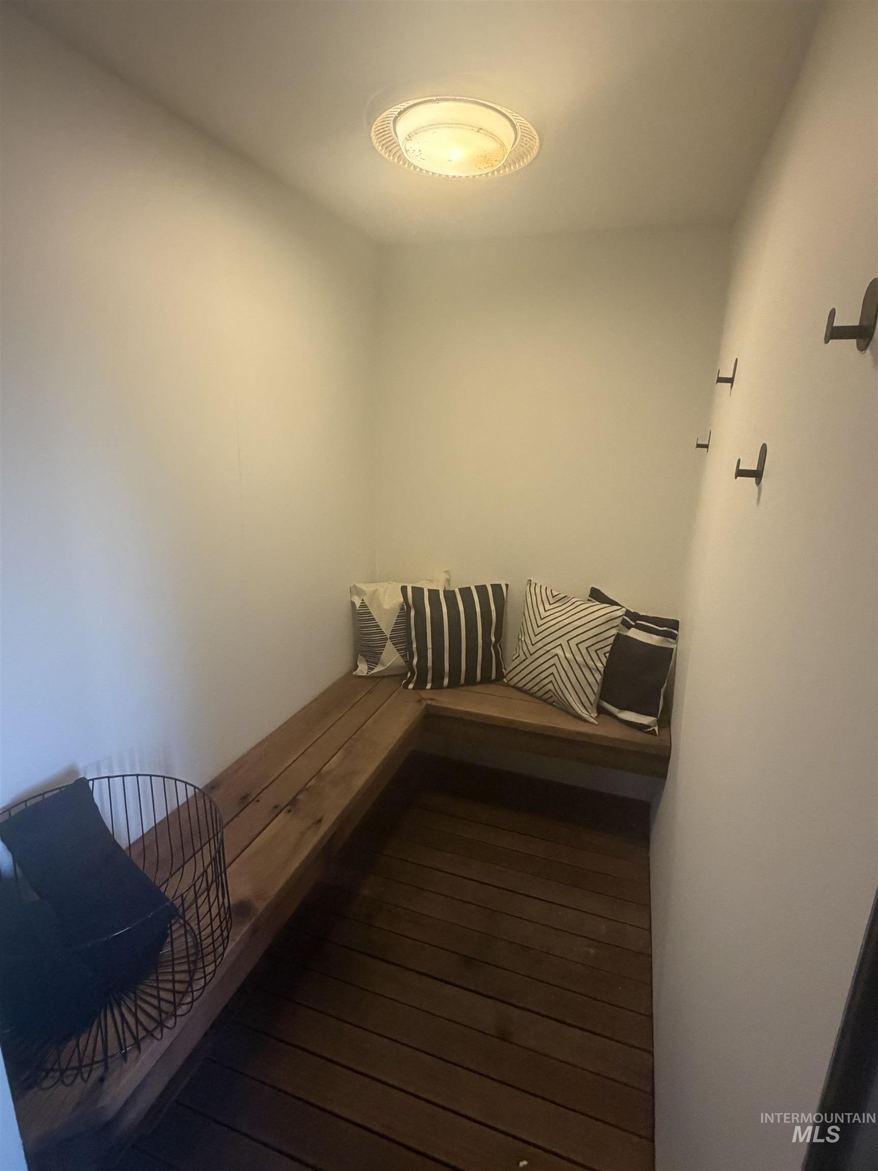 Built-in L-shaped bench seating with wood-finish planks, dark wood-finish flooring, and wall-mounted hooks