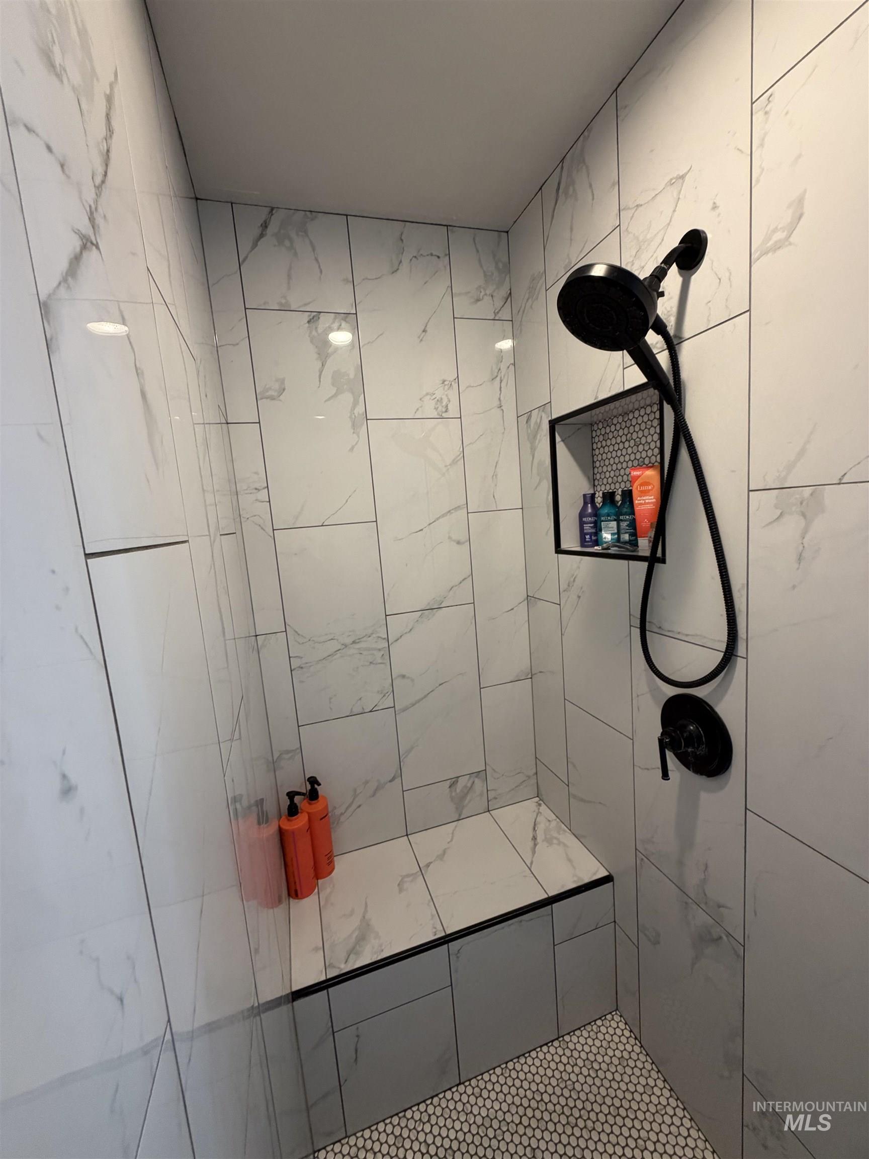 Walk-in shower featuring large format white and grey marbled tile walls, a built-in bench with a contrasting black trim, and a matte black shower fixture