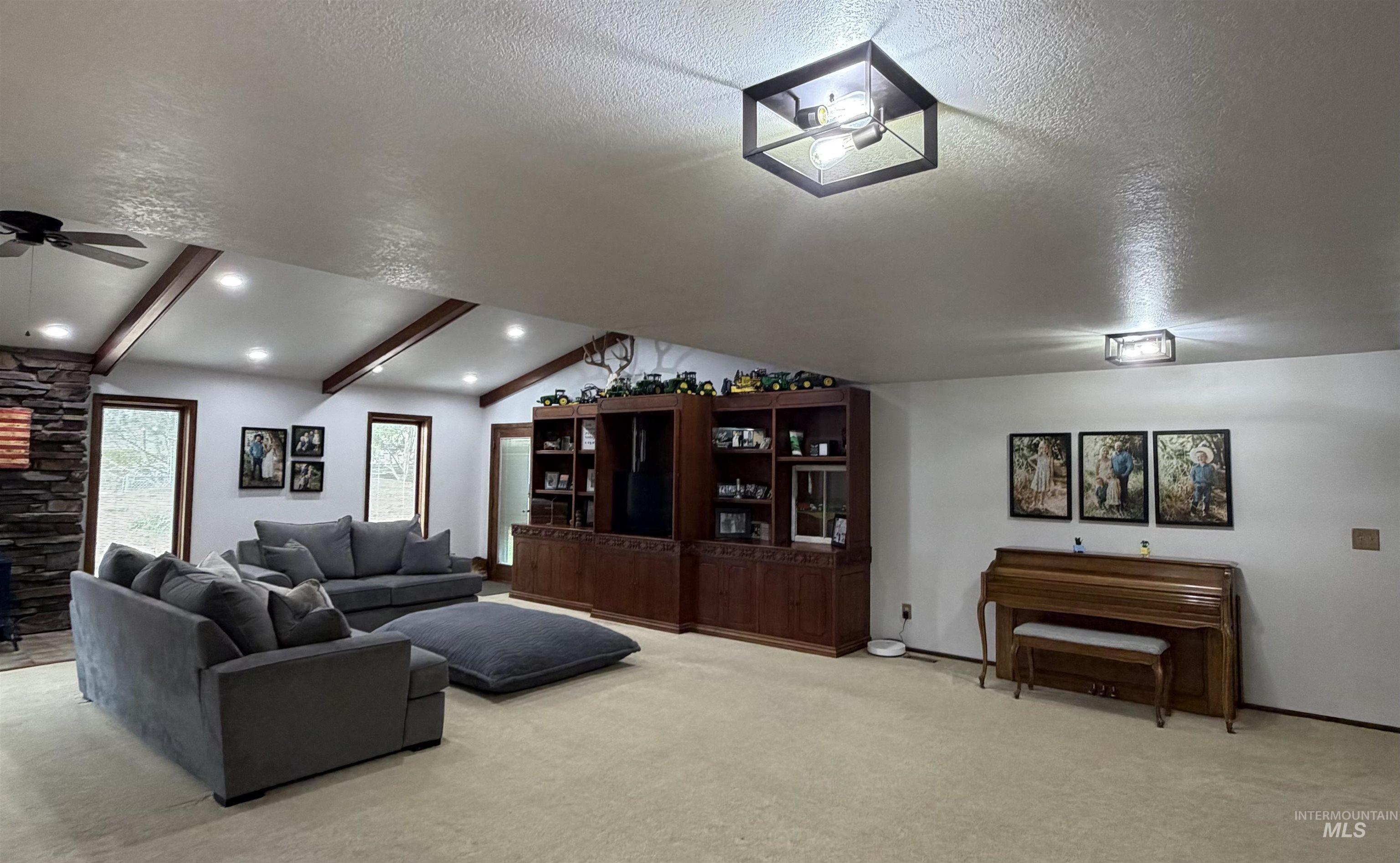 Spacious living area featuring a vaulted ceiling with exposed wood beams, recessed lighting, and a stone fireplace