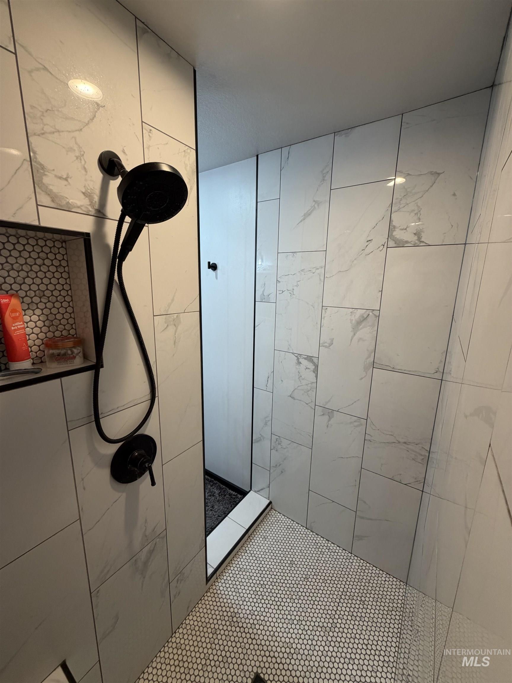 Shower with white marble-look subway tile walls, black matte shower fixtures, and a built-in recessed niche featuring a mosaic penny tile backer