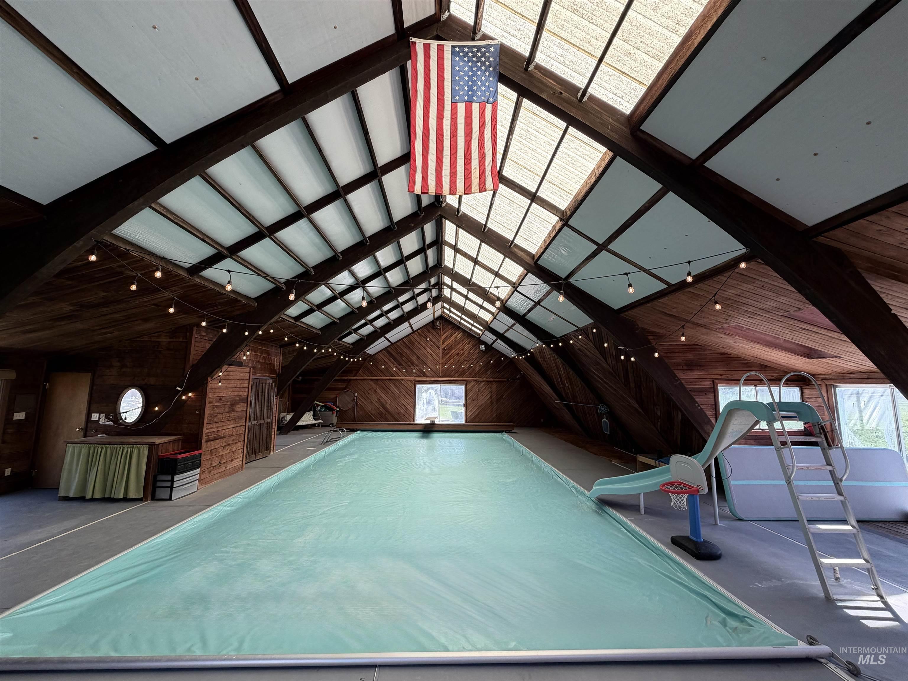 Indoor swimming pool area featuring a gabled roofline with skylight panels, exposed wood beams, and wood-paneled walls