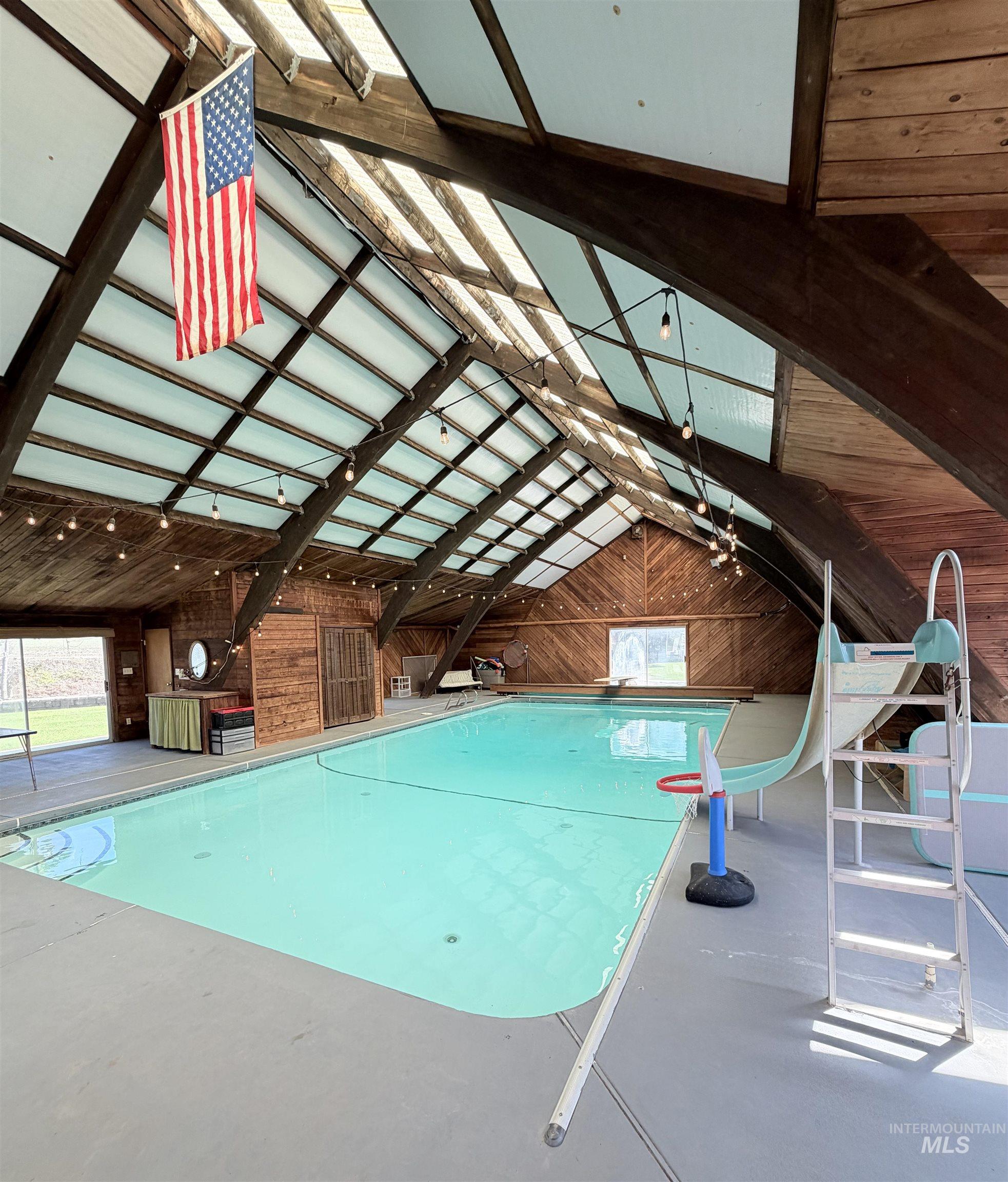 Indoor swimming pool featuring a vaulted wood-paneled ceiling with skylights, exposed wood beams, and string lighting