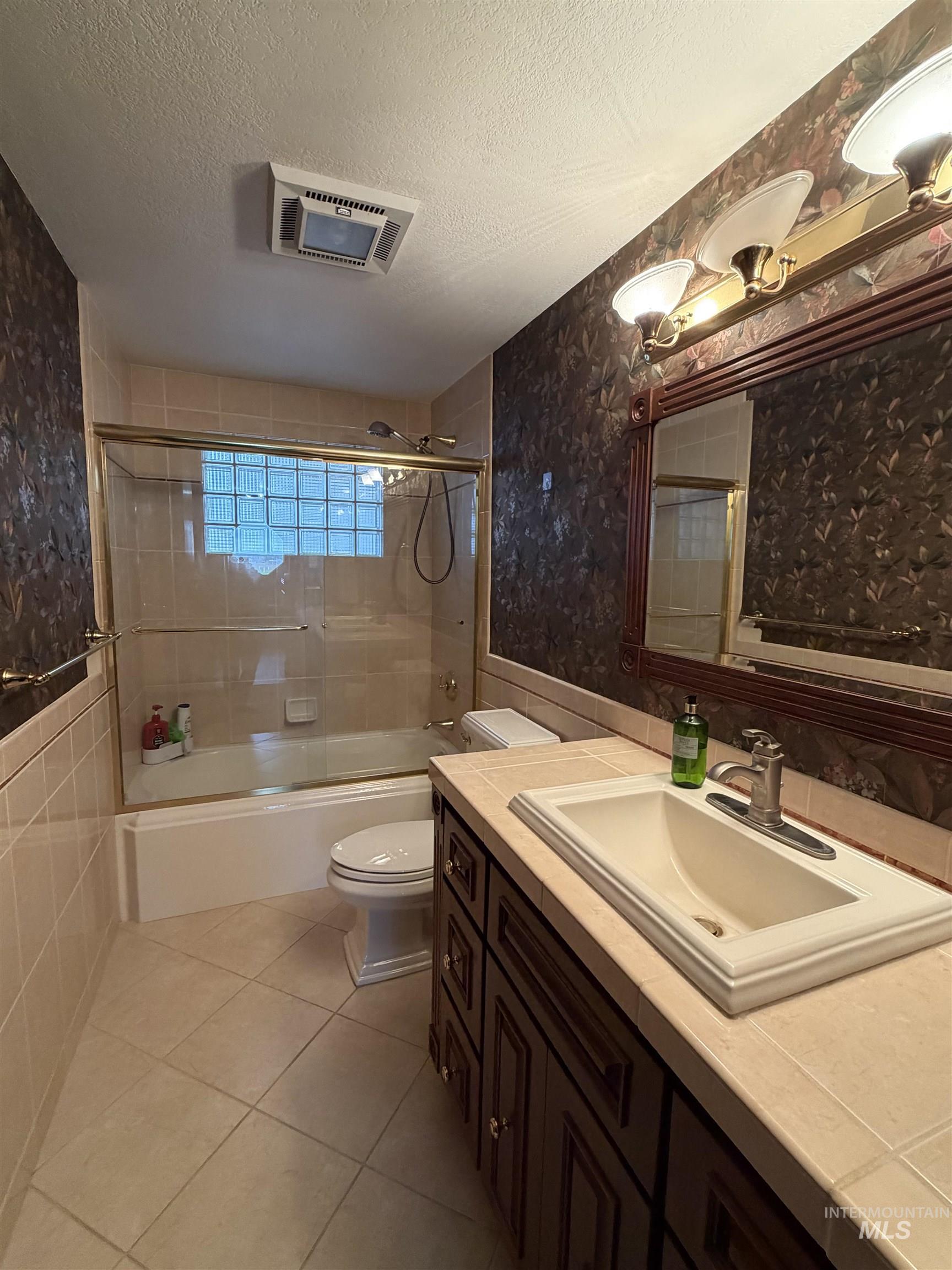 Bathroom featuring a dark wood-finish vanity with an integrated sink, a tiled countertop, and a vanity mirror with overhead lighting
