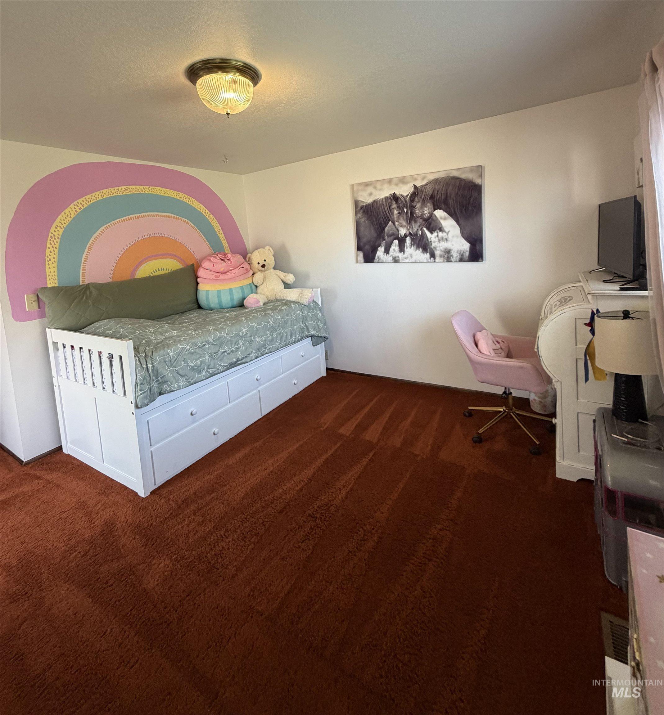 White walls with a decorative rainbow mural, brown carpeting, and a white built-in daybed with integrated storage drawers