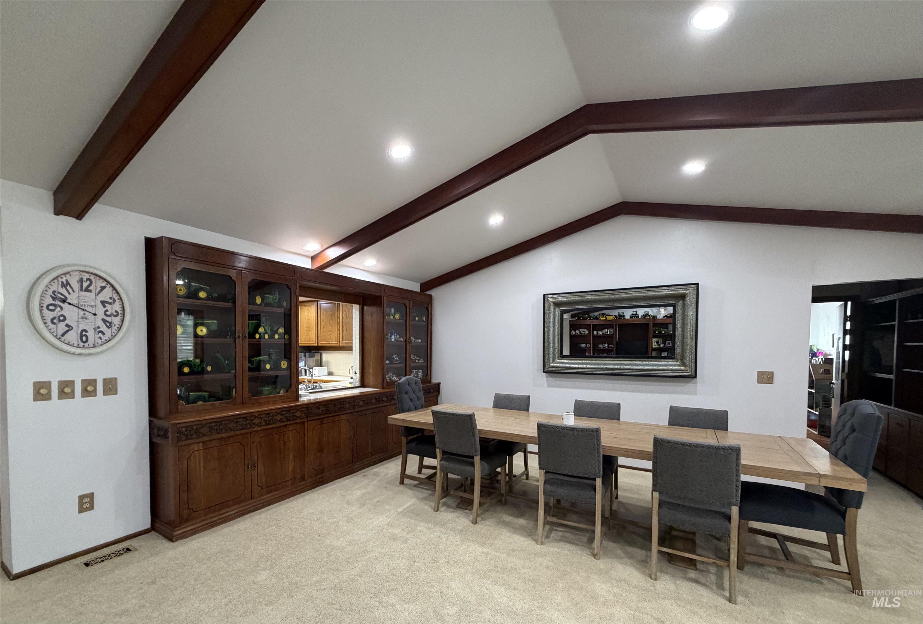 Vaulted ceiling with exposed wood beams, recessed lighting, and a built-in wood display cabinet featuring glass doors and carved details