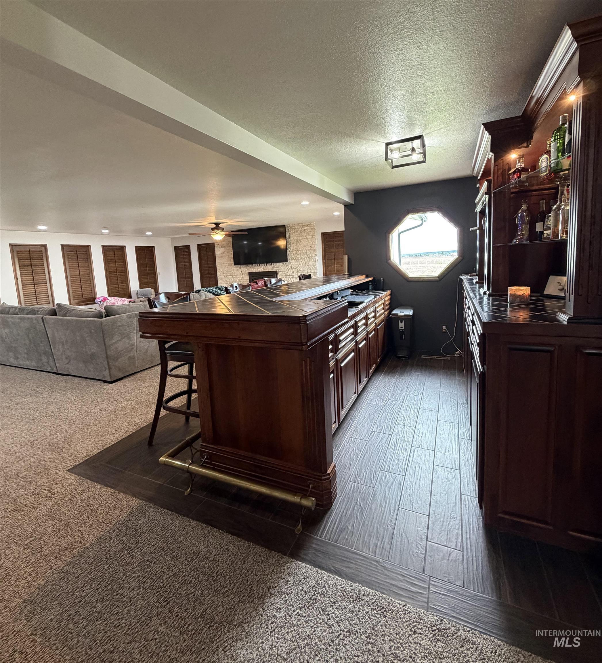Custom built-in bar featuring wood cabinetry, a tiled countertop, and an octagonal window