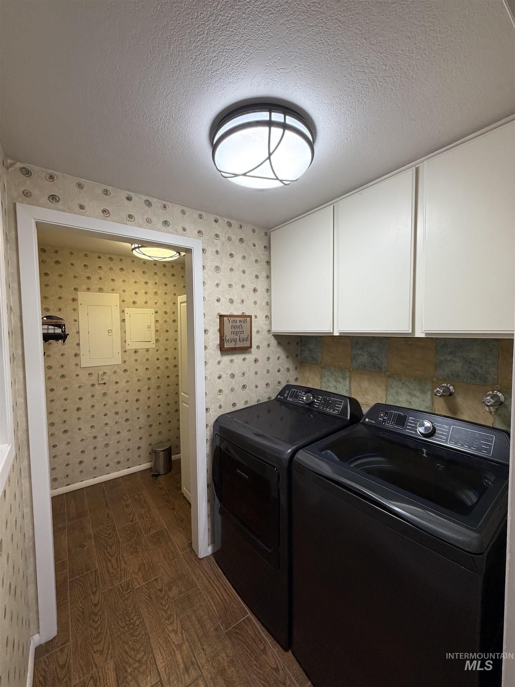Laundry area featuring wood-finish flooring, white upper cabinetry, and a patterned wall covering
